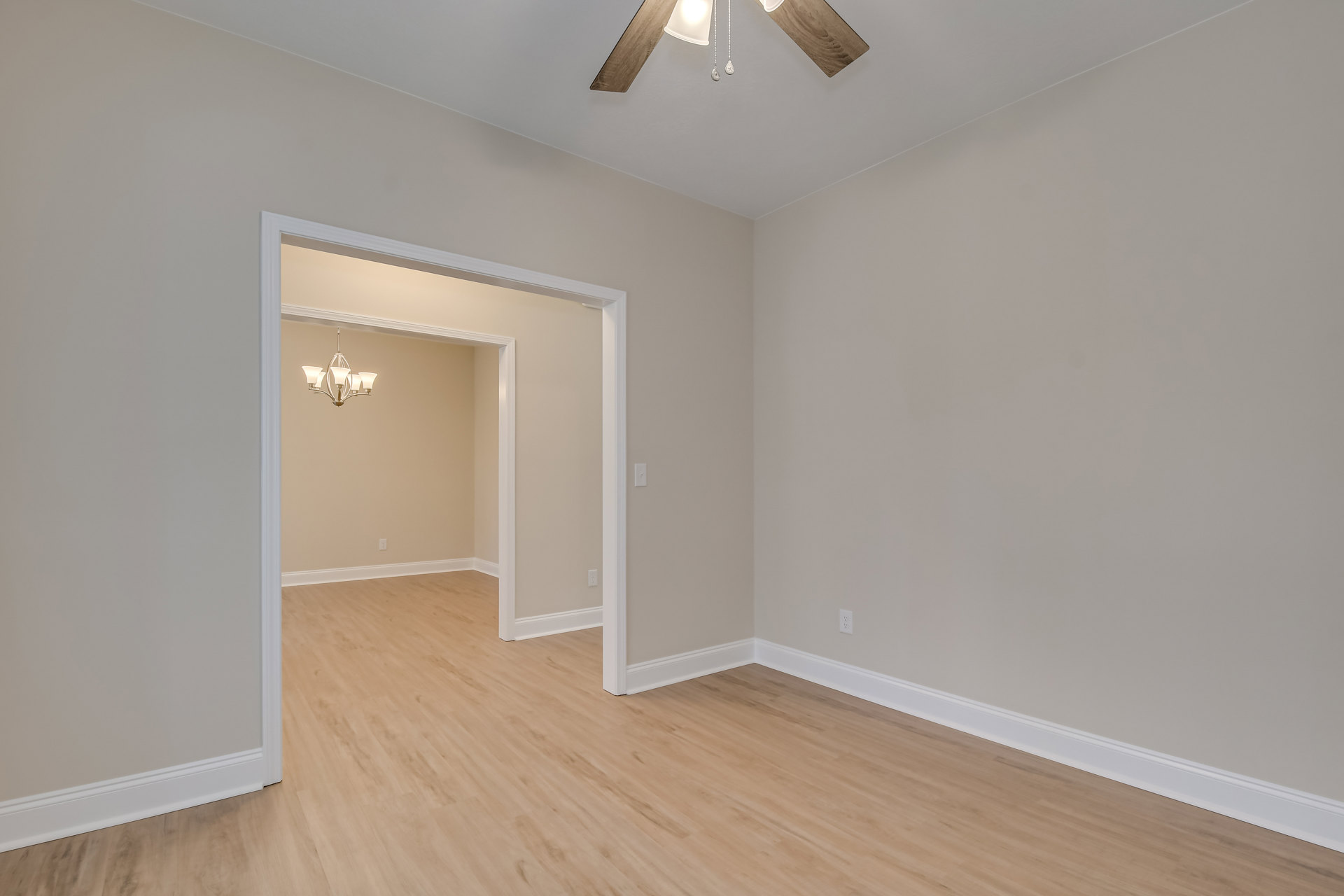White-walled room with wood flooring, ceiling fan, chandelier, and white door