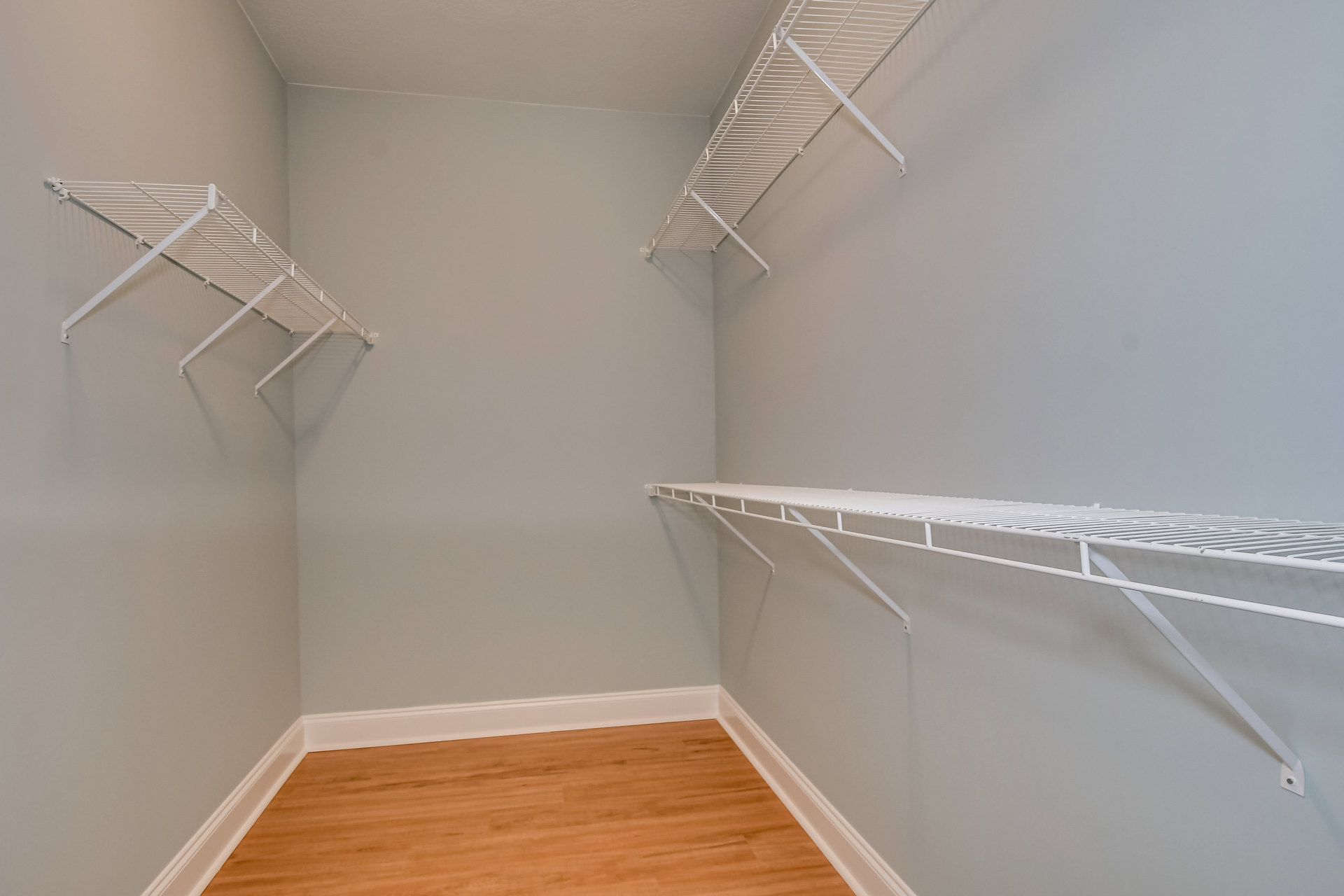 Hardwood floor with white baseboard, built-in white shelves along wall, plaster ceiling, and molding accents in a custom closet room