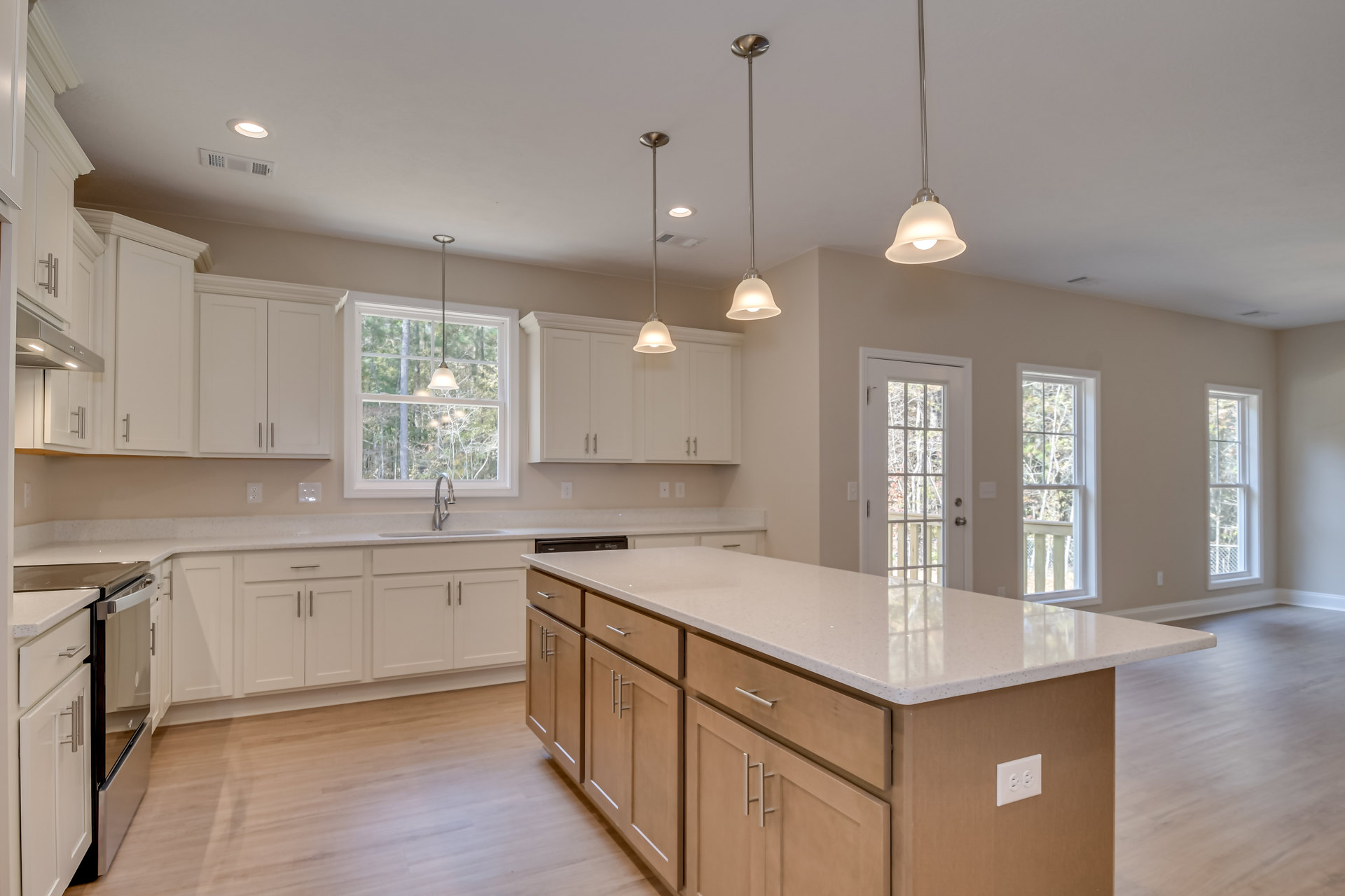Spacious kitchen featuring a large marble-topped island, wood flooring, white cabinetry, stainless steel appliances, glass-paneled door, and windows overlooking leafy trees