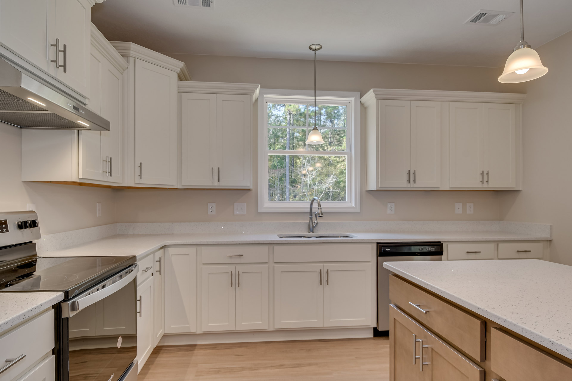 White kitchen cabinets with brushed nickel hardware, quartz countertop, stainless steel sink beneath a large window, pendant light fixture hanging from a white ceiling, integrated