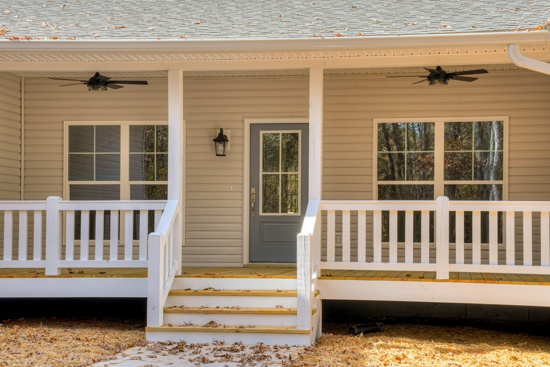 Front exterior of a house with wooden siding, two porches featuring white railings, a window with a white frame, and a door with a glass panel and handle.