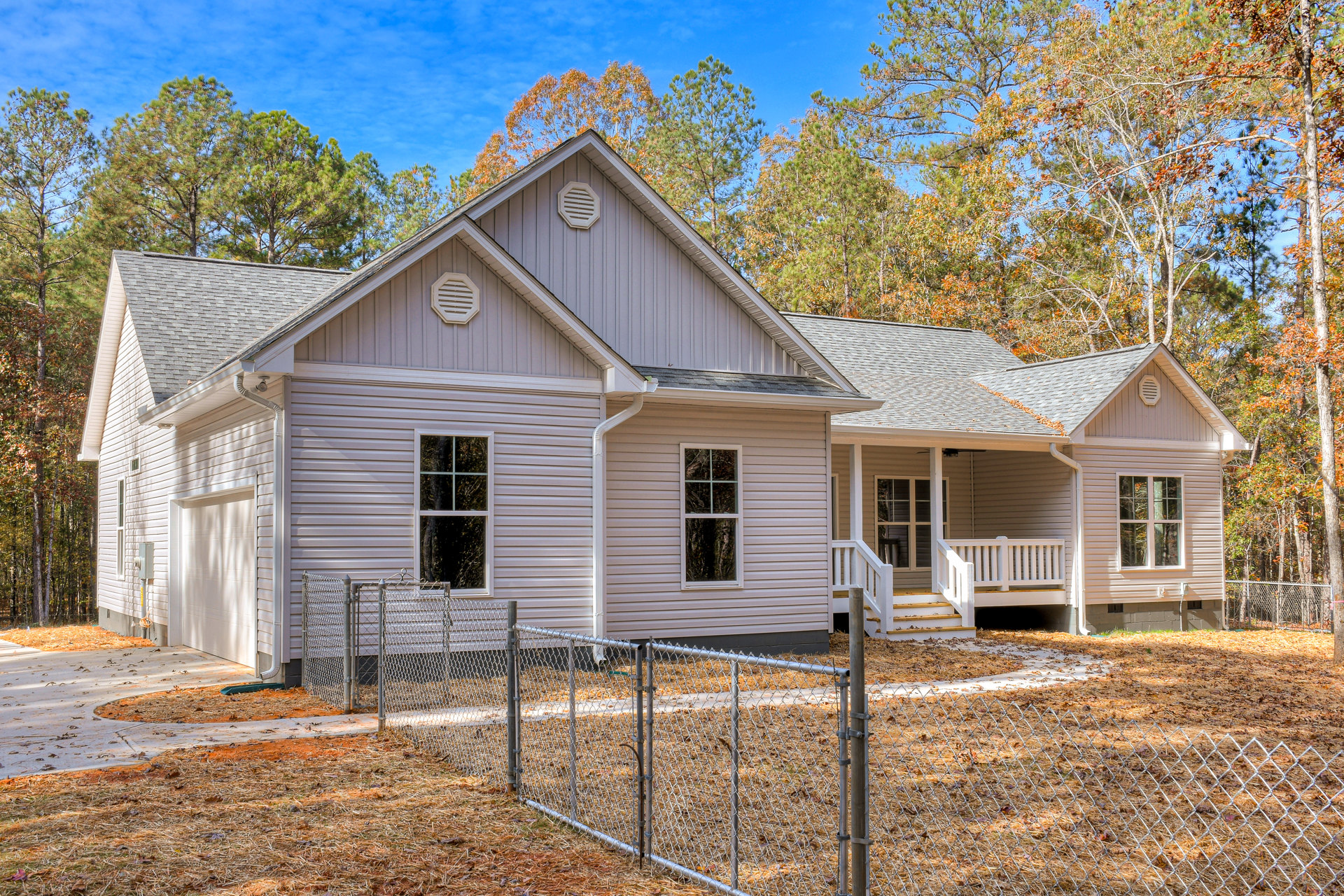 Two-story house with light siding, white-framed windows, and a covered porch with white railing; fenced yard and mature trees in the background.