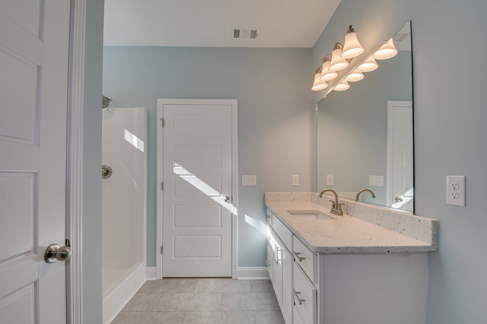 Modern bathroom featuring a white ceramic sink with chrome faucet, frameless mirror above, tiled shower enclosure, and white door with silver handle
