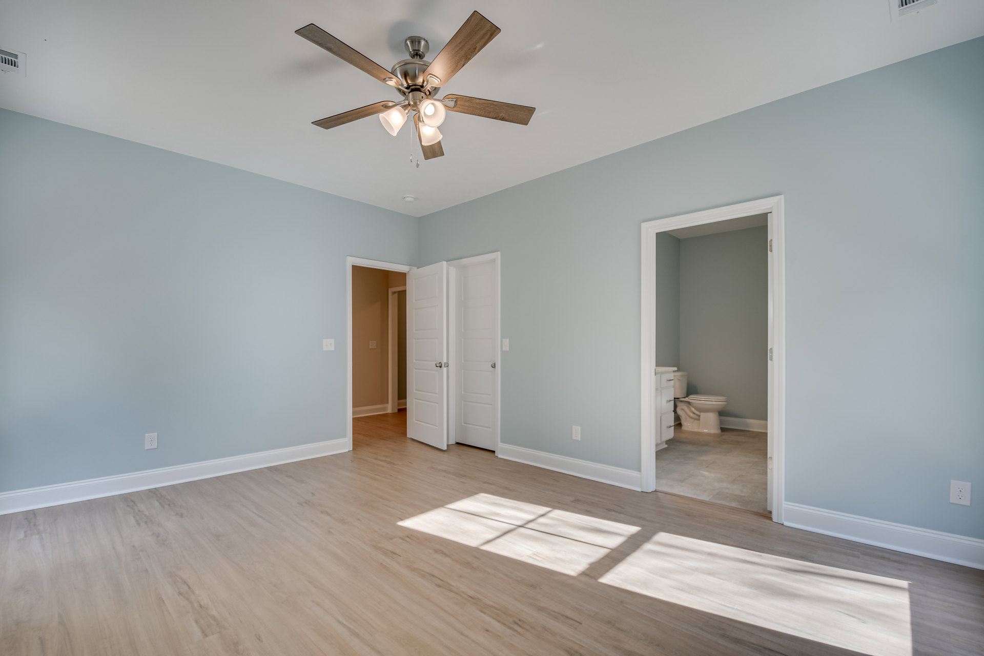 Ceiling fan with lights above hardwood floor, white toilet, white door with silver handles, light gray walls, crown molding