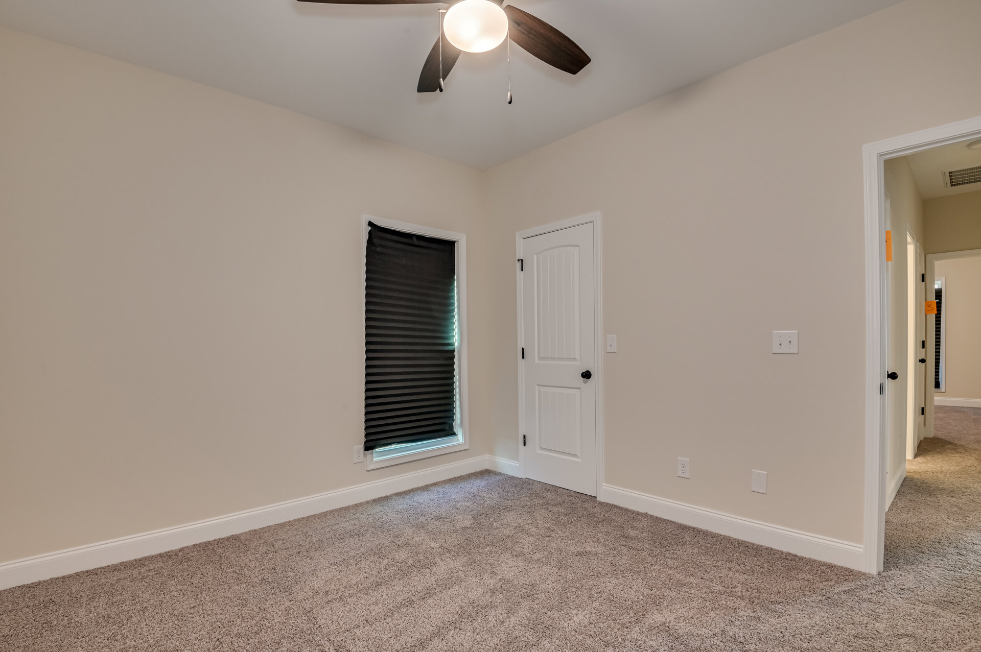 Carpeted room with white walls, black window blinds filtering sunlight, white door with black knob, ceiling fan with integrated light fixture