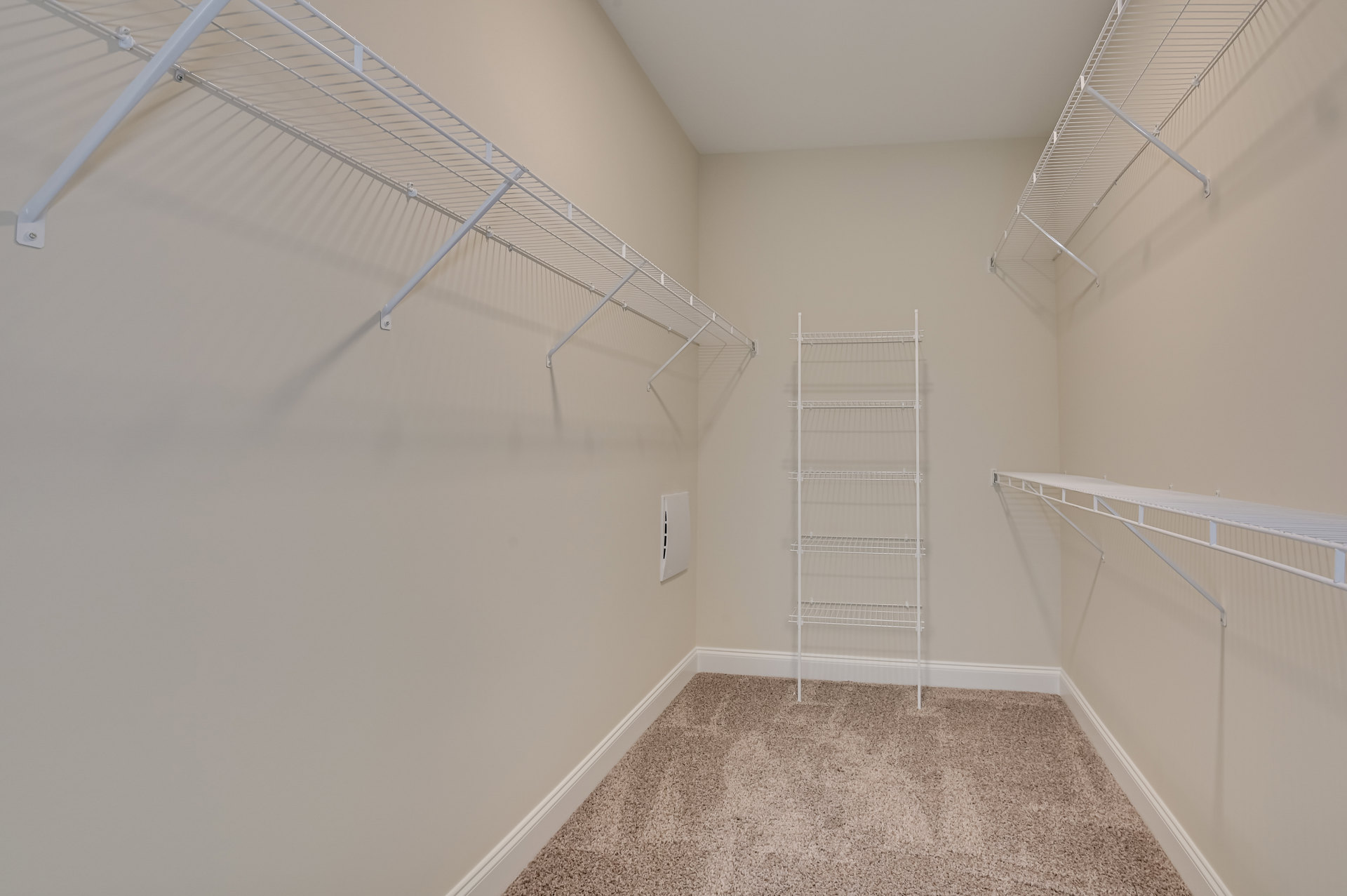 Empty walk-in closet with white metal shelving, carpeted floor, white walls, ceiling vent, and a small ladder.