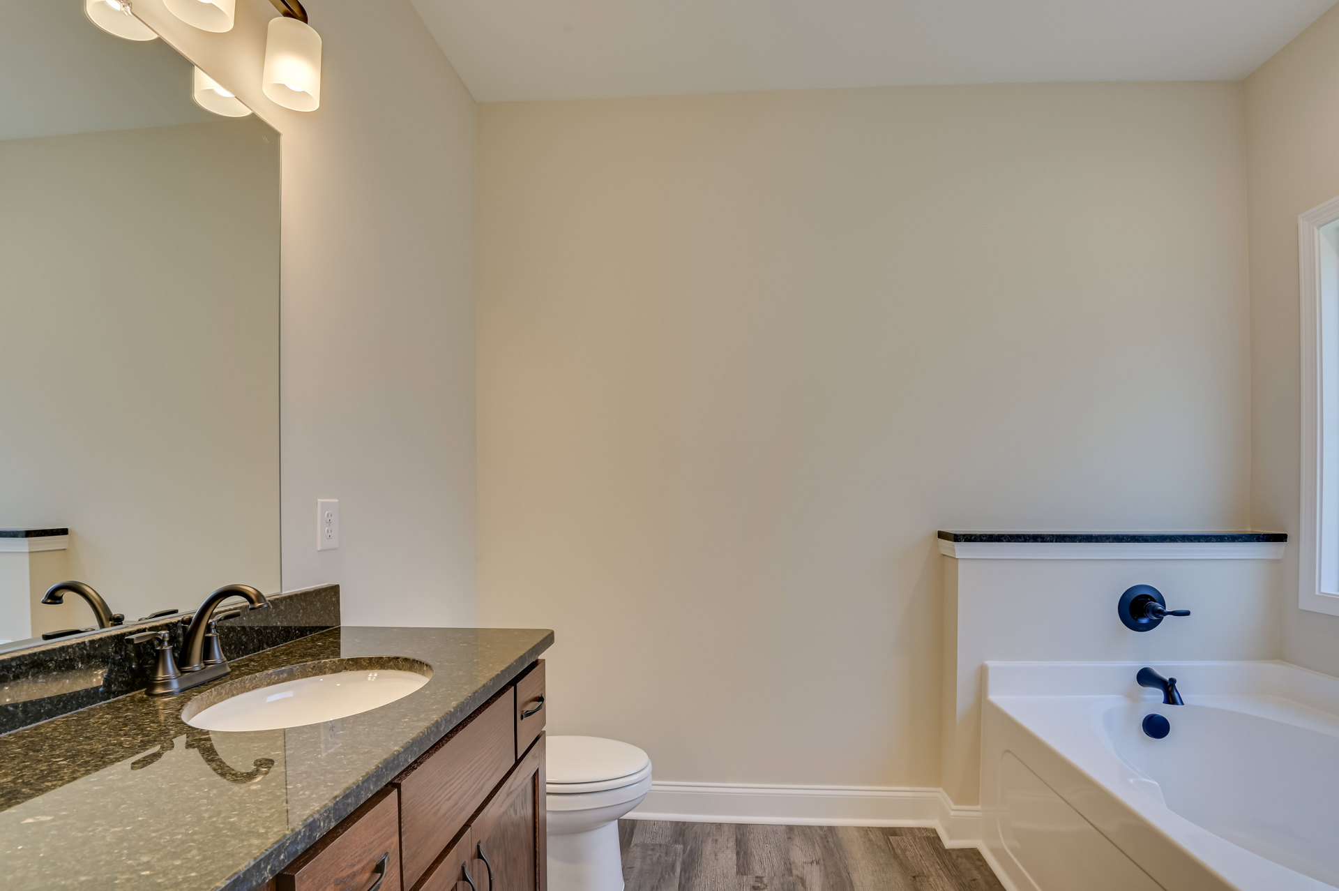 Bathroom with white freestanding bathtub and matte black faucet, white toilet, light-colored vanity with sink and chrome faucet, large wall mirror, ceiling-mounted light fixtures