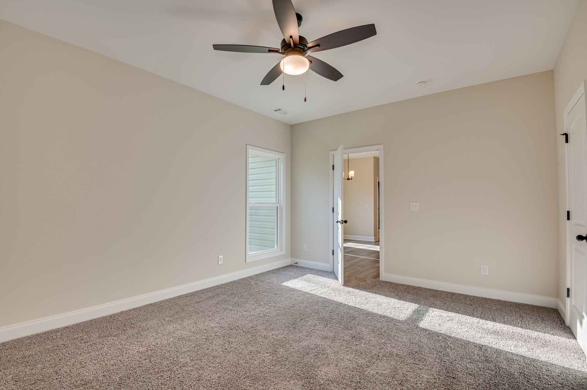 Carpeted room with white walls, ceiling fan with light fixture, window with white trim, and a paneled door