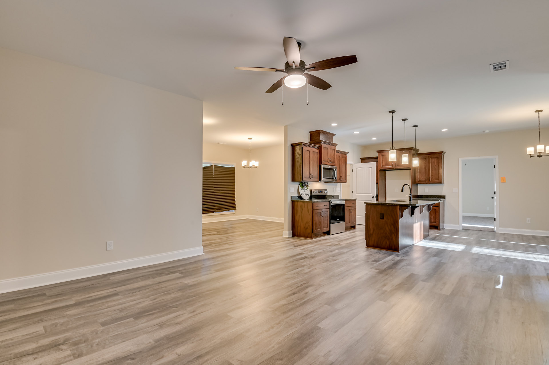 Open-concept kitchen and living room featuring wood laminate flooring, white walls and ceiling, ceiling fan with light, window with blinds, white door with black handle, built-in
