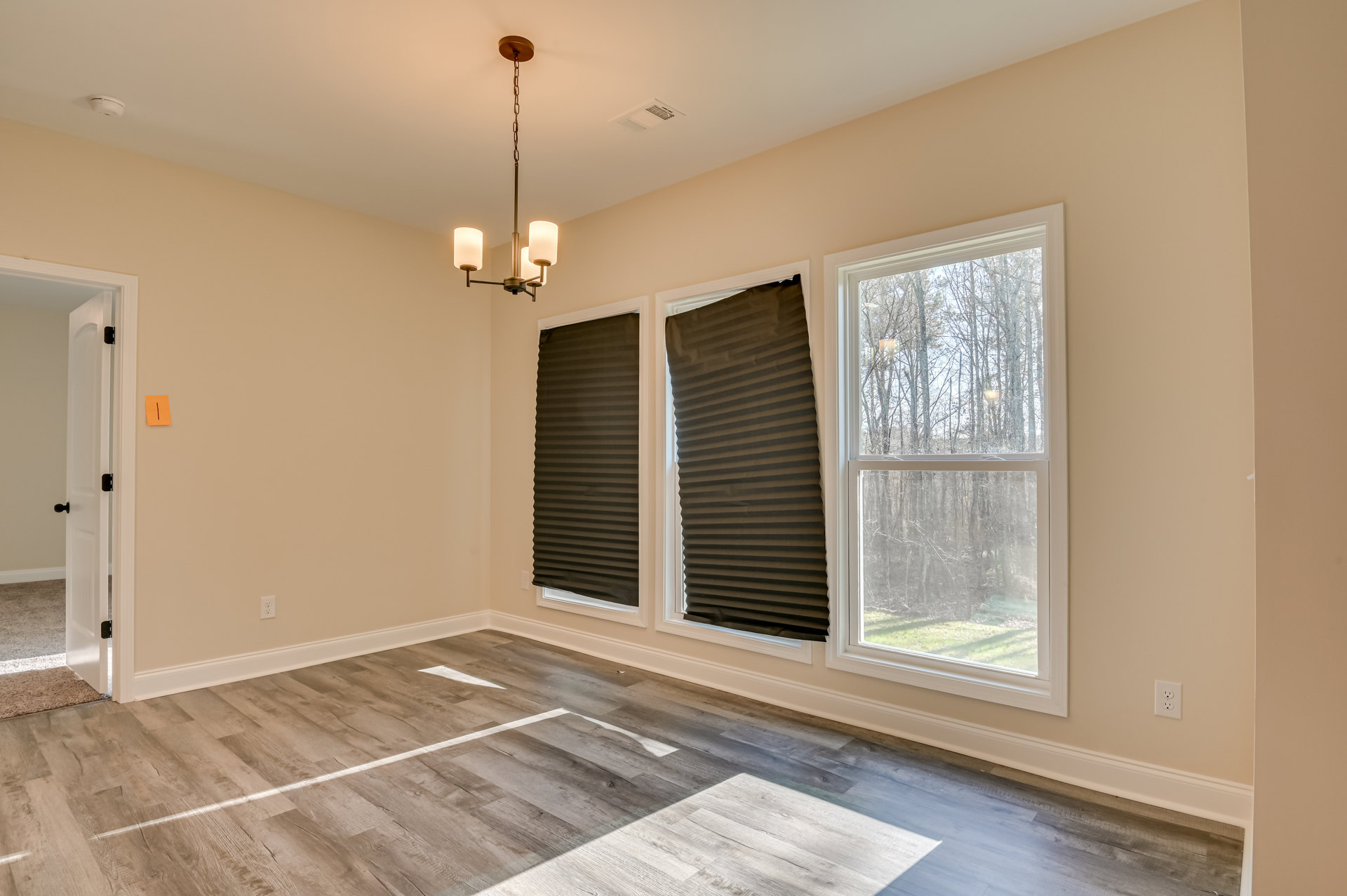 Spacious room with wood flooring, large windows framed by black and brown blinds, chandelier hanging from plaster ceiling, trees visible outside