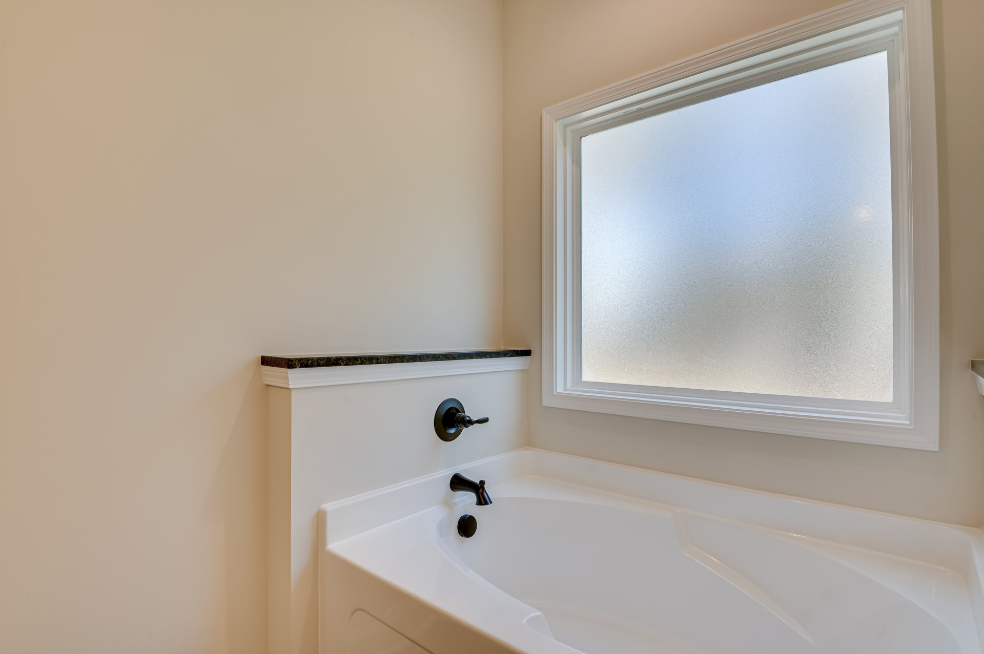 White freestanding bathtub beneath frosted window, chrome faucet and wall-mounted switch, light-colored bathroom walls