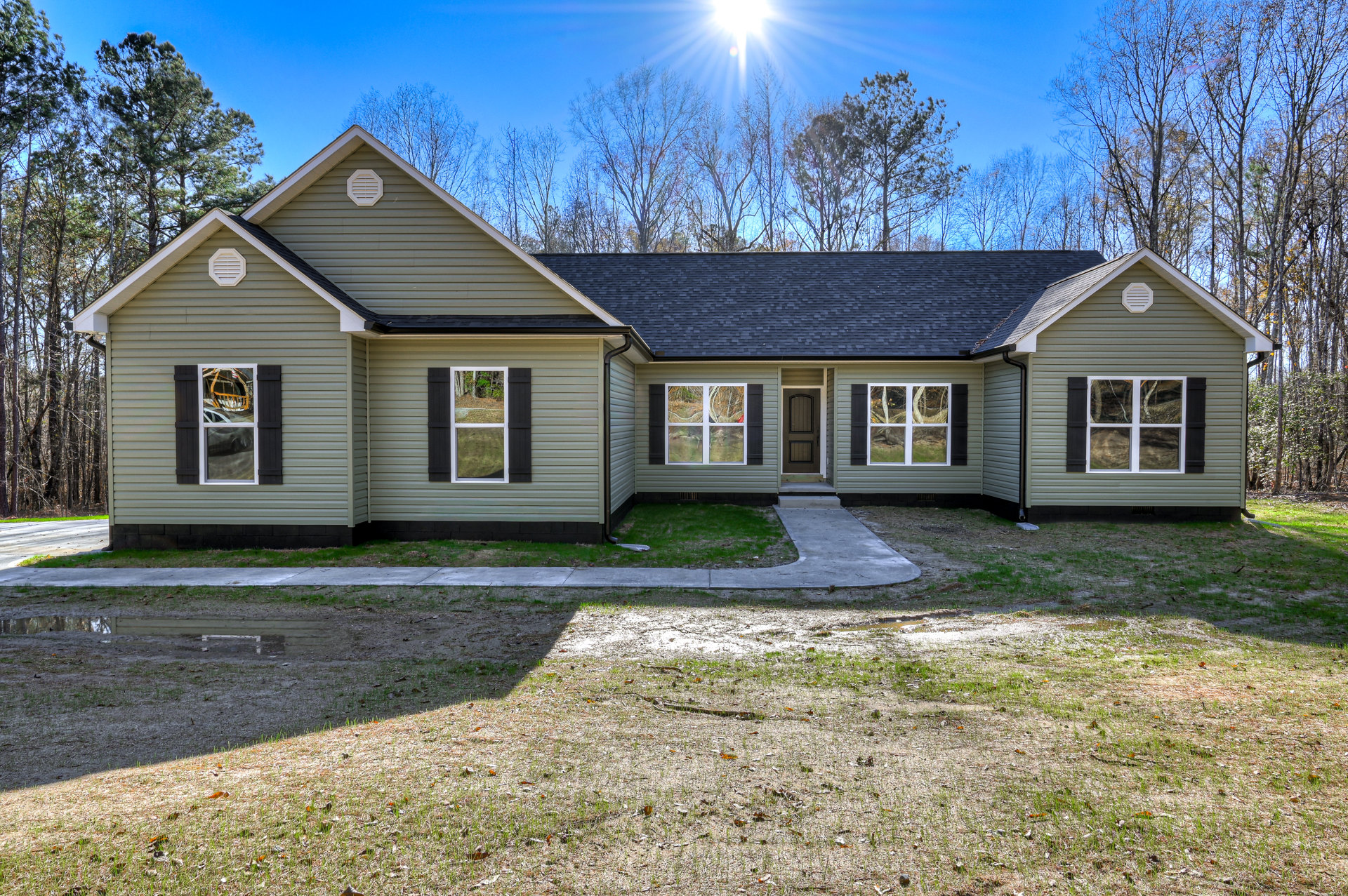 Modern two-story home with gray siding, large windows reflecting trees, covered porch, manicured lawn, concrete driveway, and mature trees in the yard