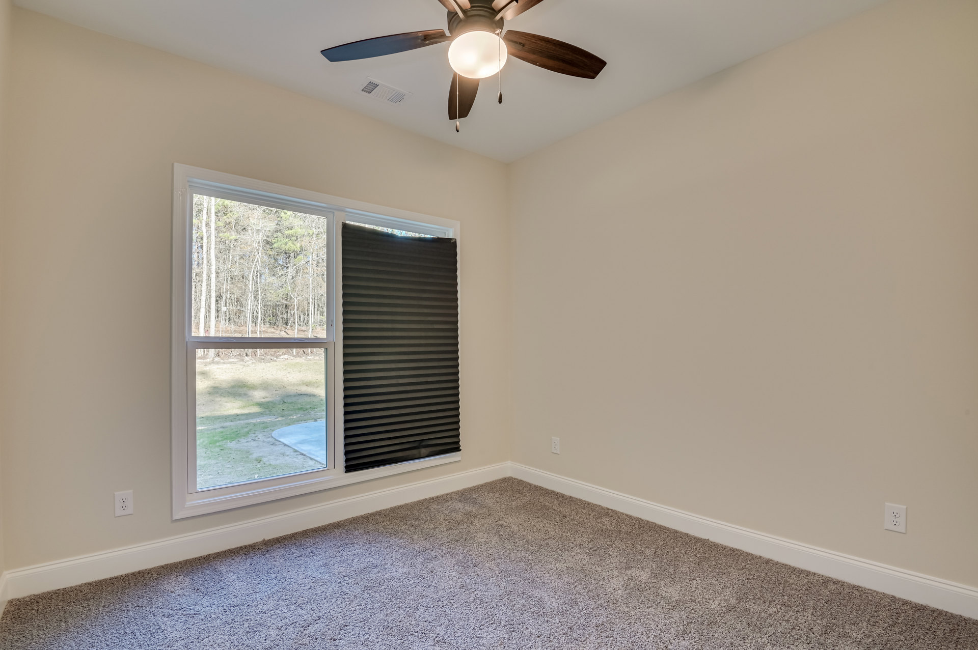 Carpeted room with white walls, ceiling fan with light fixture, large window featuring black blinds