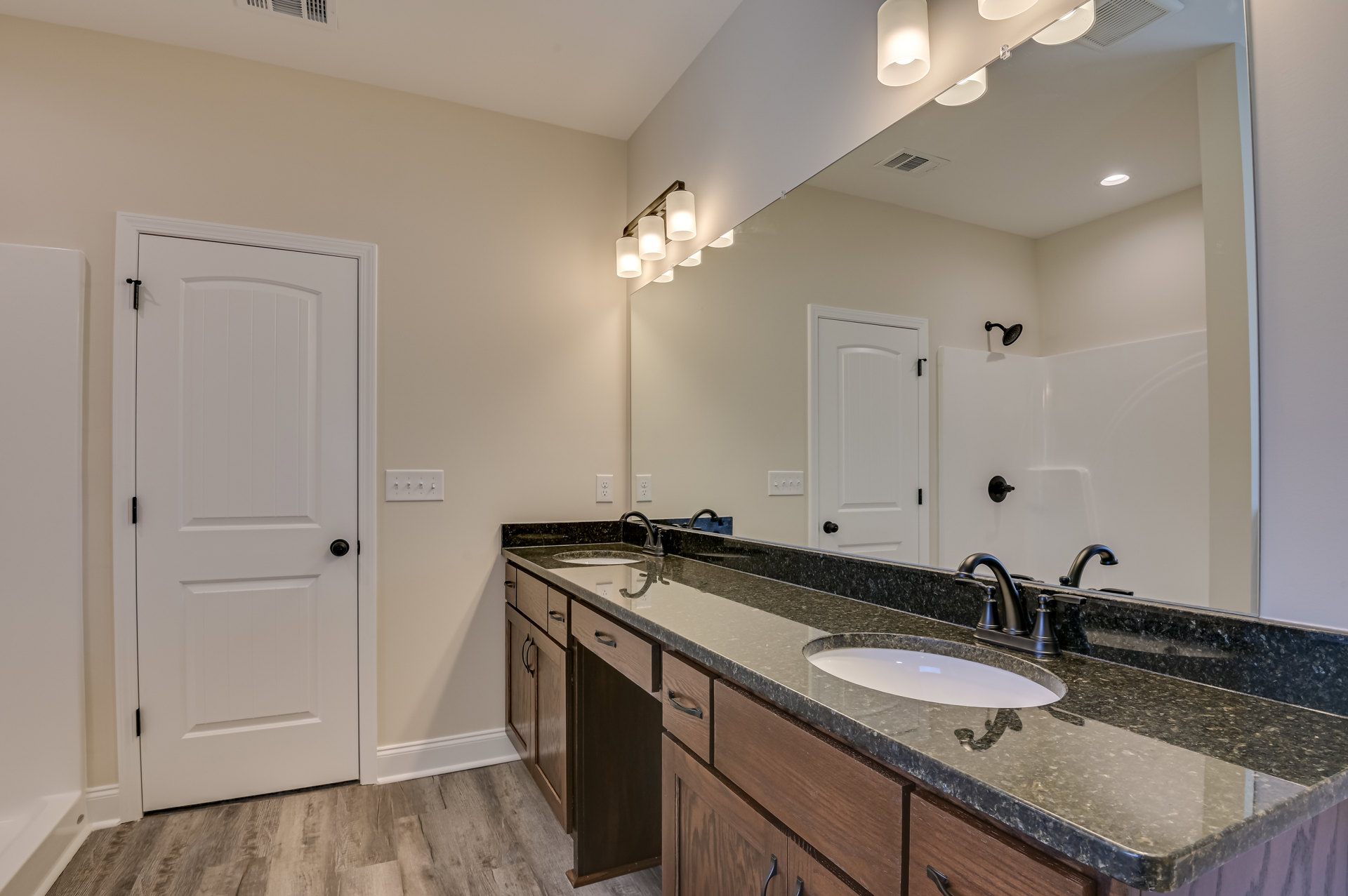 Double vanity bathroom with white cabinets, black hardware, large frameless mirror, chrome faucets, and light-colored countertop.