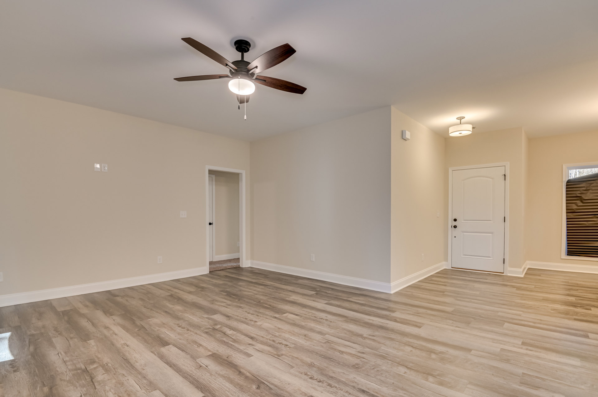 Ceiling fan with light fixture mounted on white ceiling, wood plank flooring, white doors with black and silver doorknobs, neutral walls, framed brown artwork.