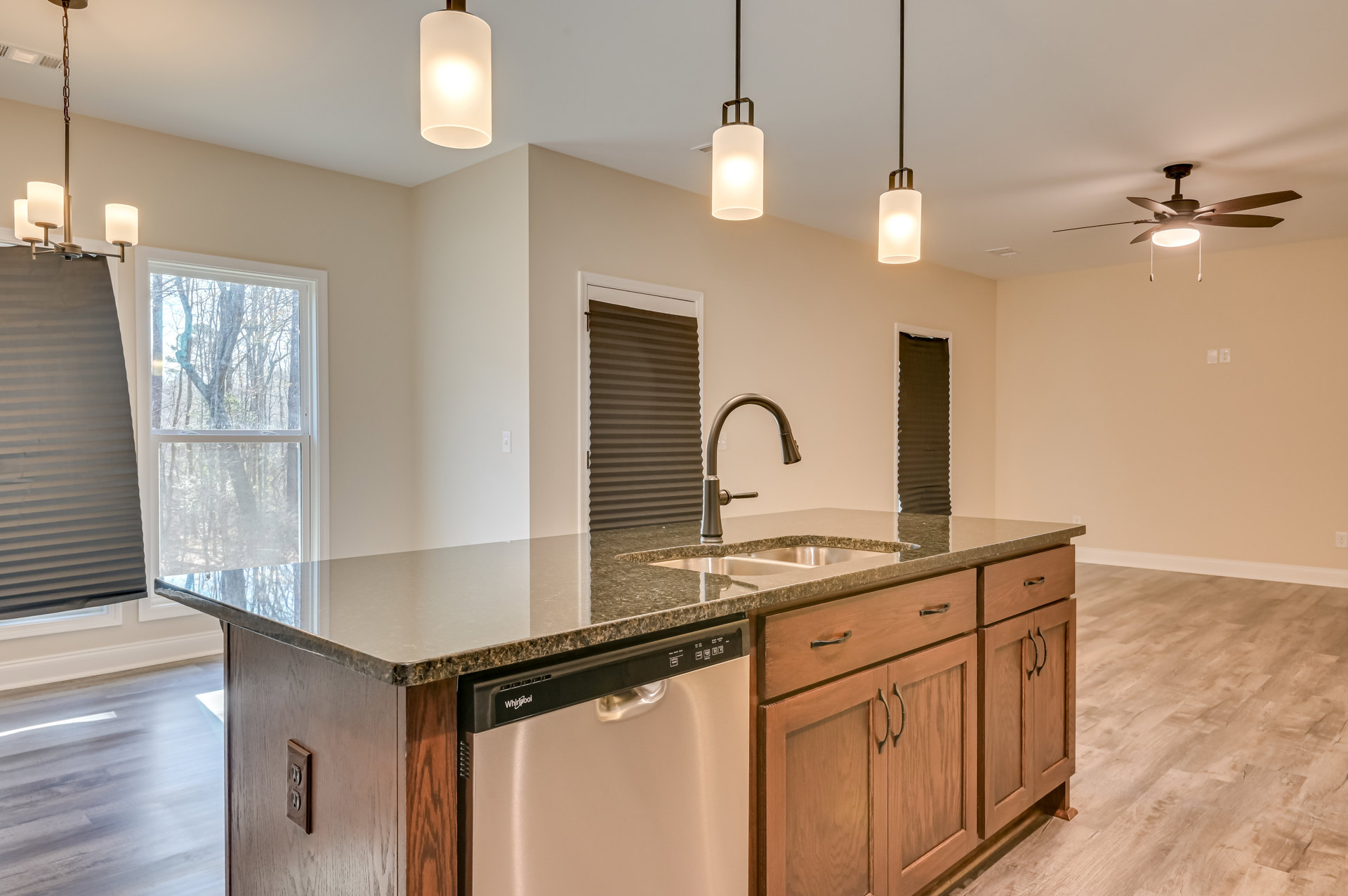 White quartz countertop with undermount sink, stainless steel dishwasher, white shaker cabinets, black roller shade over window, recessed lighting illuminating workspace