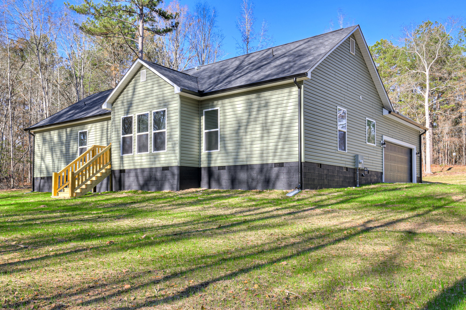 Two-story home with white-framed windows, wooden exterior stairs, attached garage with light, surrounded by green lawn and mature trees