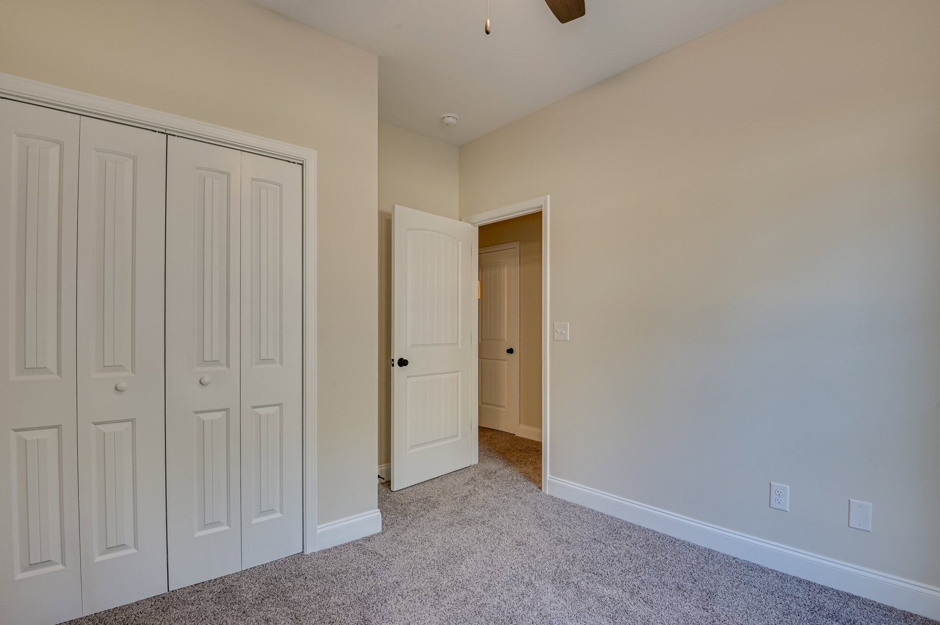 Room with white paneled doors, carpeted floor, white walls, ceiling fan, and electrical outlets