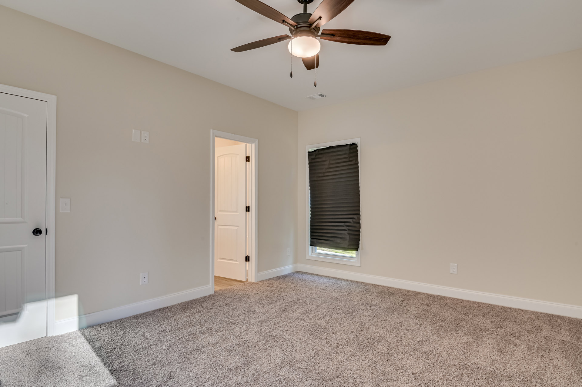 Ceiling fan with integrated light above carpeted floor, black window blinds, white door with black knob, close-up of door handle, white plaster walls