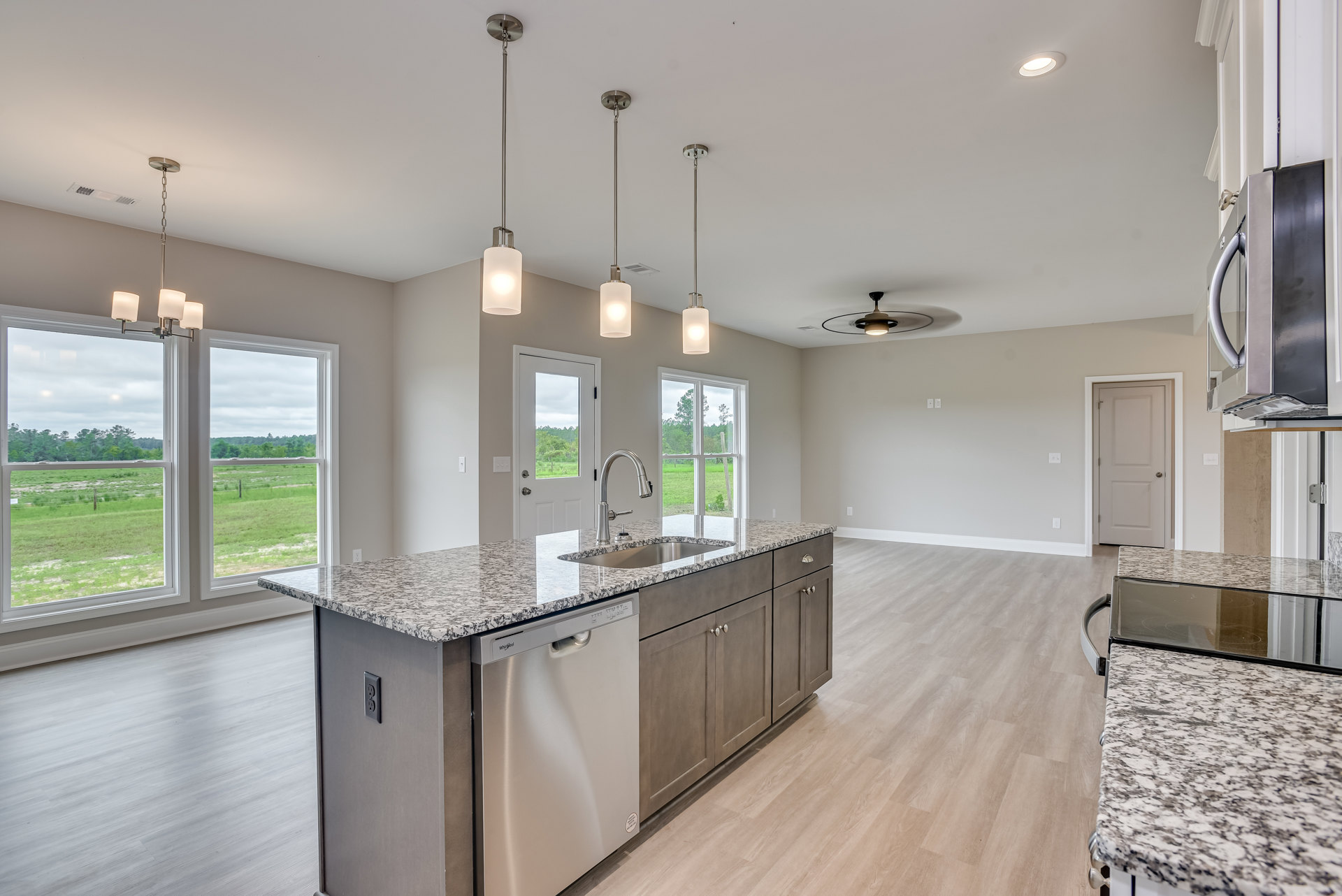 Modern kitchen with two stainless steel sinks set in a light stone countertop, white cabinetry, silver door handle, pendant light fixture, and large window overlooking a grassy