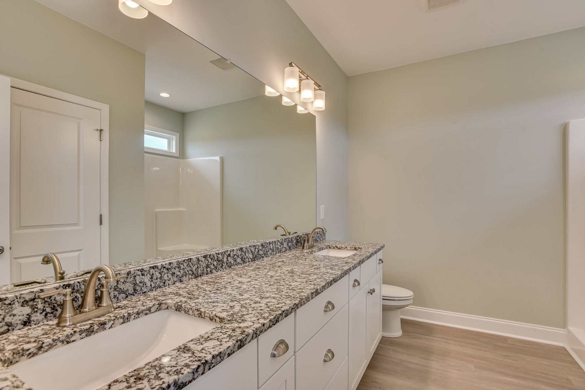 Marble countertop with undermount sink and chrome faucet, expansive wall mirror, modern light fixture, white toilet, and tiled walls in a contemporary bathroom