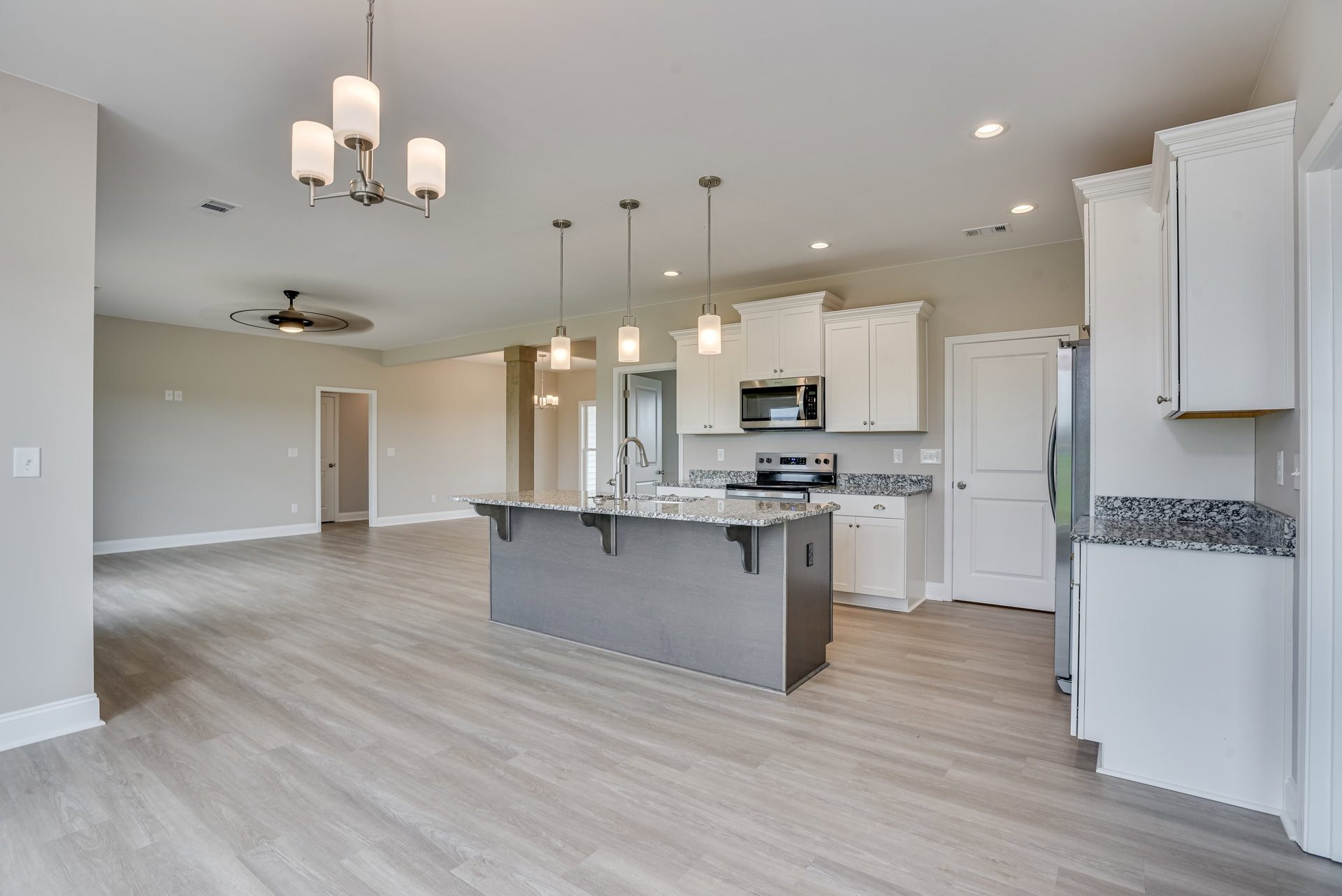 Open kitchen and dining area featuring white shaker cabinets, stainless steel microwave, stone countertops, pendant light fixtures, white paneled door, hardwood flooring, and