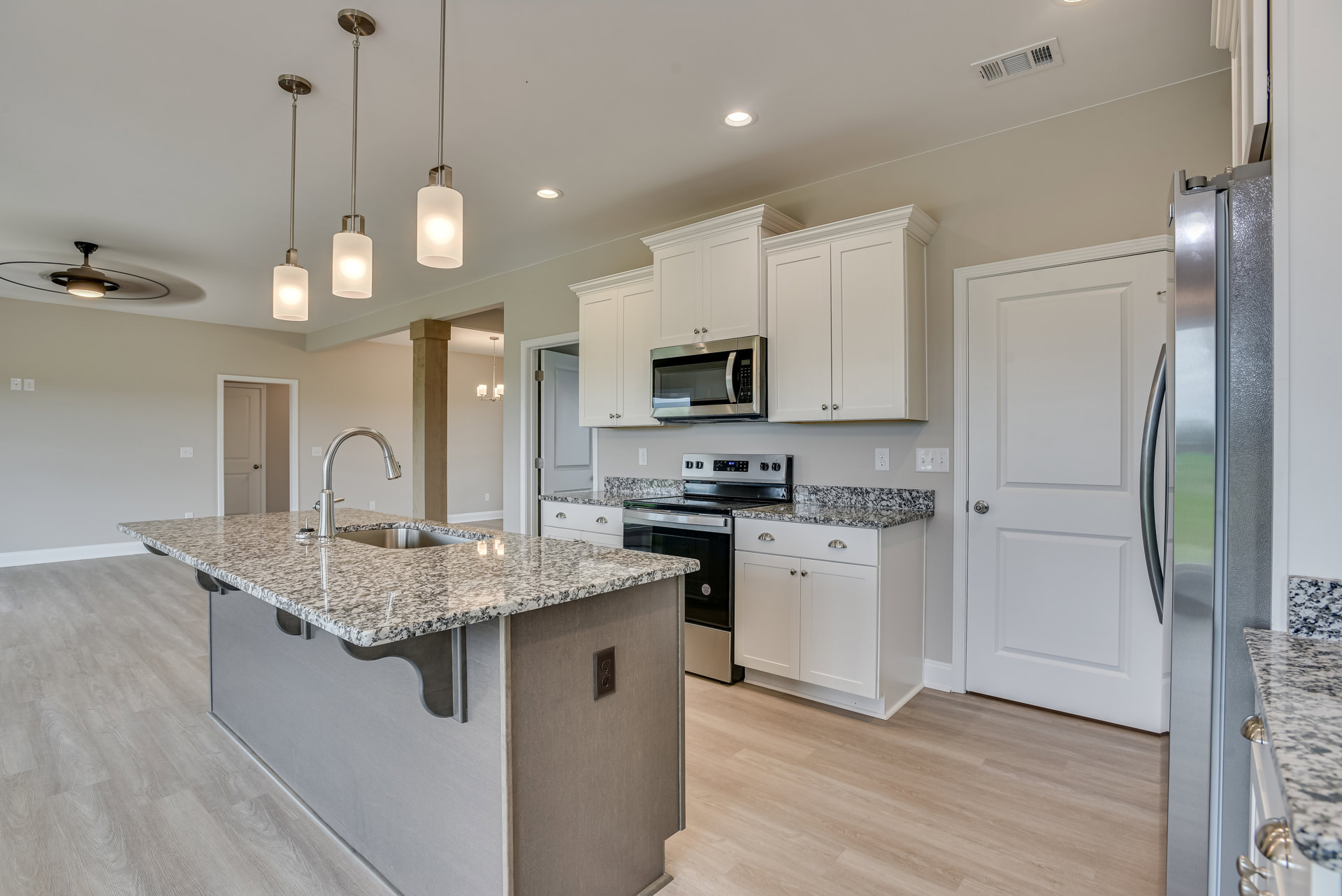 Granite countertops and white cabinets in a kitchen with a central island sink, stainless steel microwave, tile flooring, modern light fixtures, and a white door with a silver