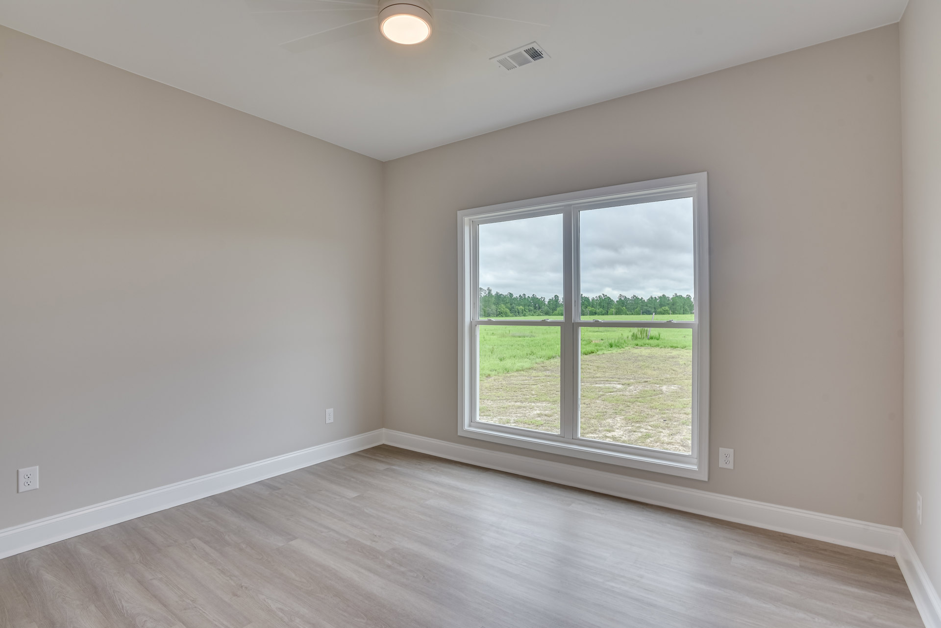 Sunlit room featuring large window overlooking grassy field and trees, smooth plaster walls, and polished wood flooring
