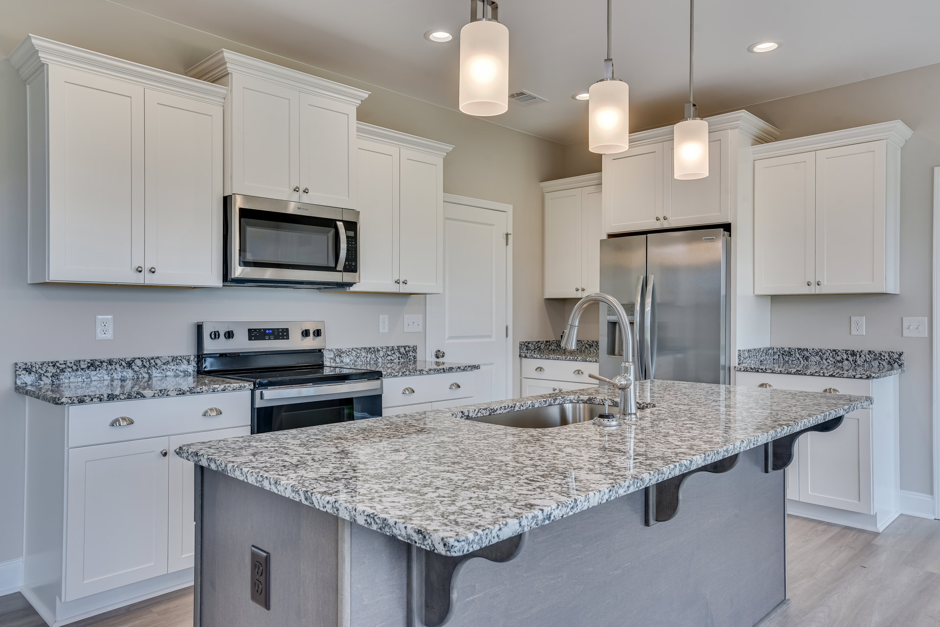 Granite countertops and white cabinetry in a modern kitchen with stainless steel refrigerator, built-in microwave, undermount sink, and rectangular ceiling light fixture