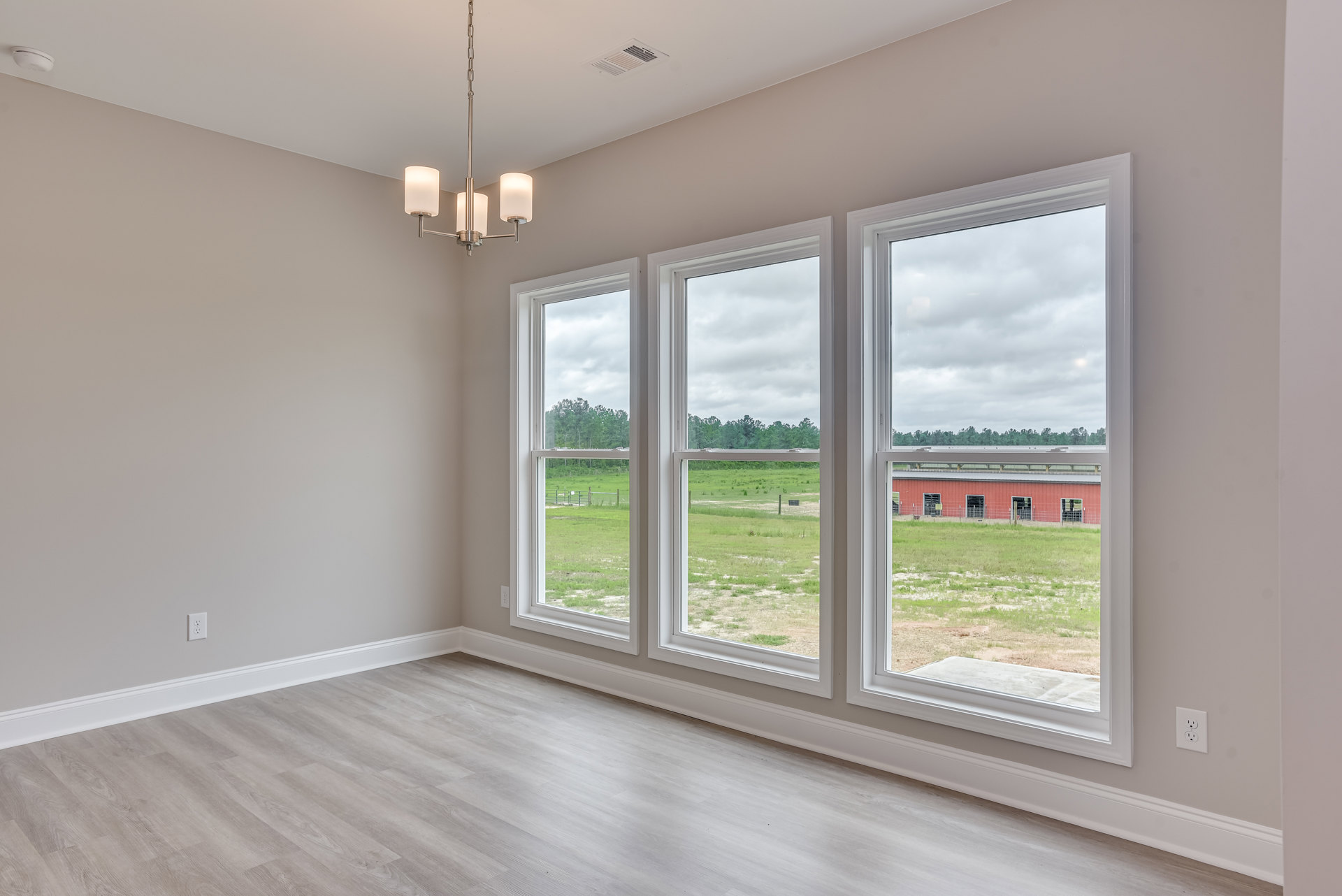 Bright room with large windows overlooking grassy field, white floors, ceiling vent, and modern lamp