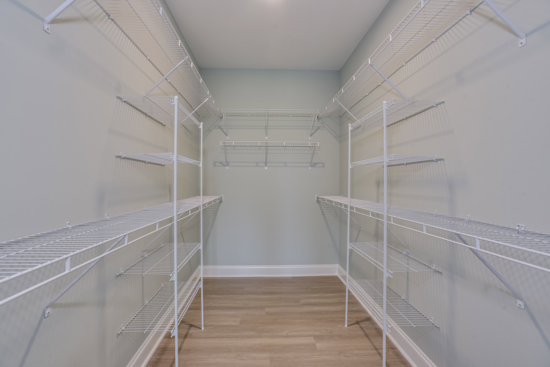 Closet with white built-in shelves, wood flooring, and plaster ceiling