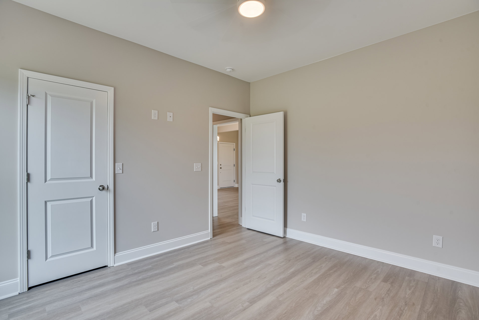 Room with wood flooring, white paneled doors featuring silver handles, white walls with crown molding, and a ceiling fan with light fixture