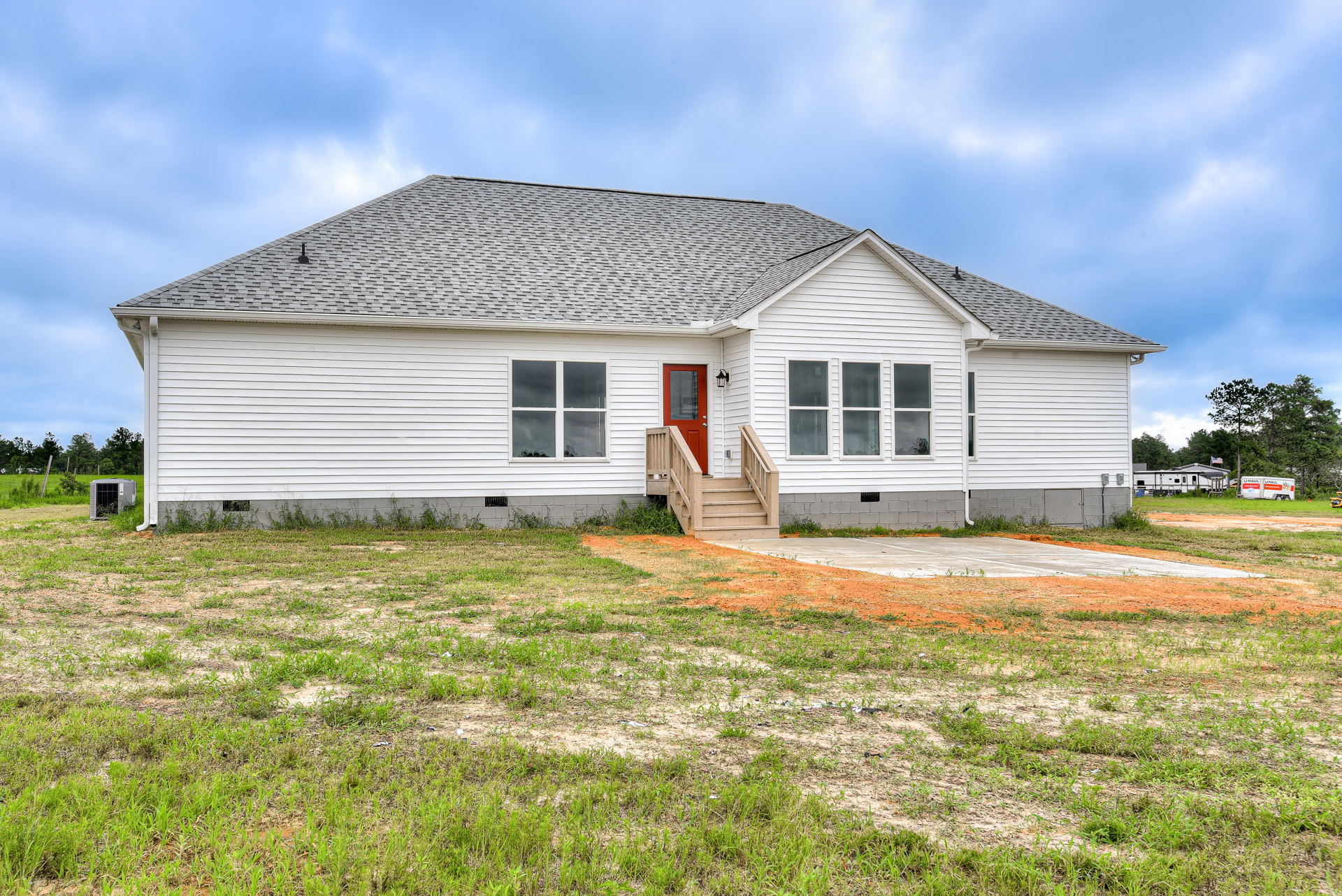 White siding house with red front door, wooden staircase, white-framed windows, and green lawn under partly cloudy sky