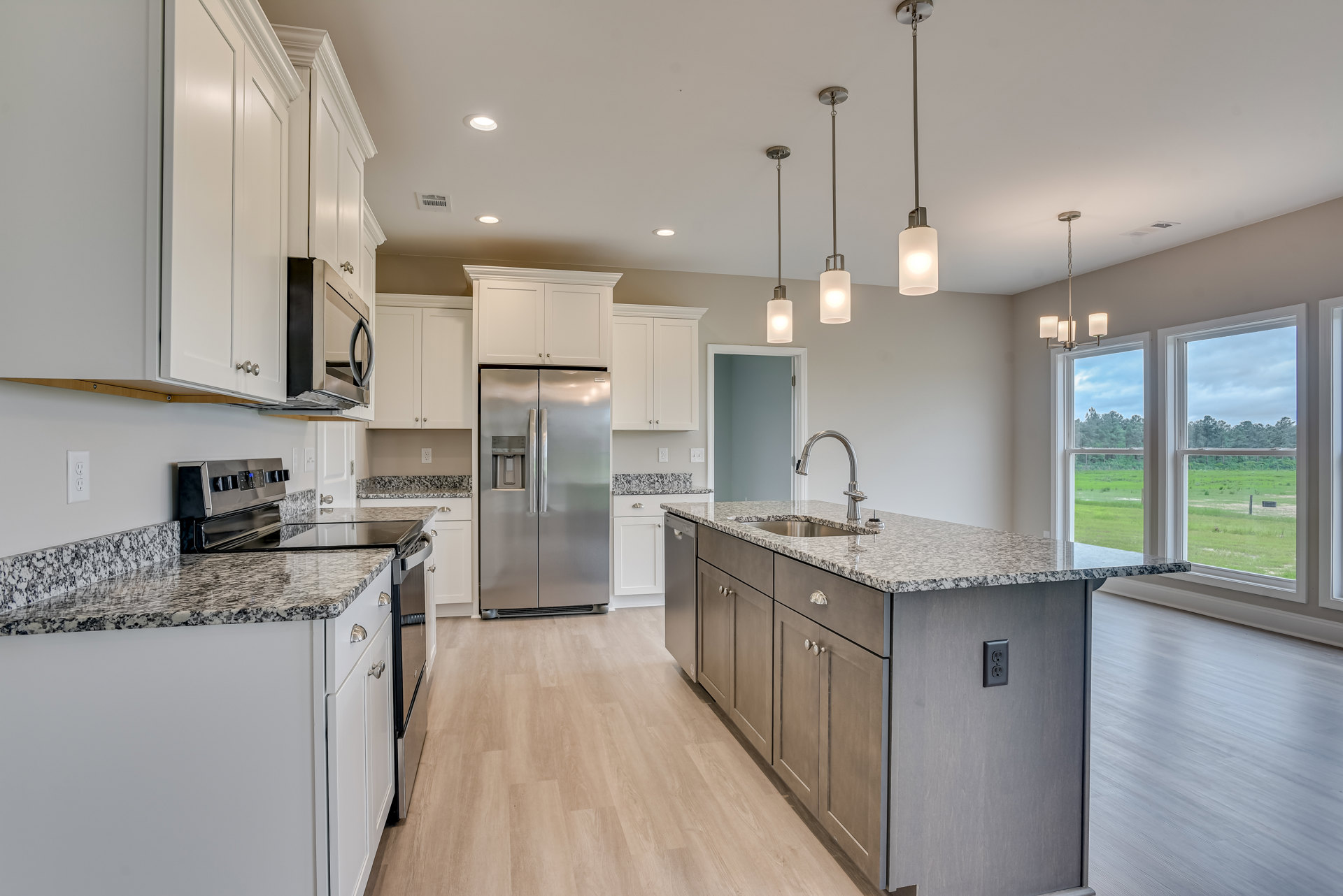 Granite countertops, stainless steel refrigerator with water dispenser, white cabinetry, metal faucet, light wood flooring, and wooden door frame in a modern kitchen.