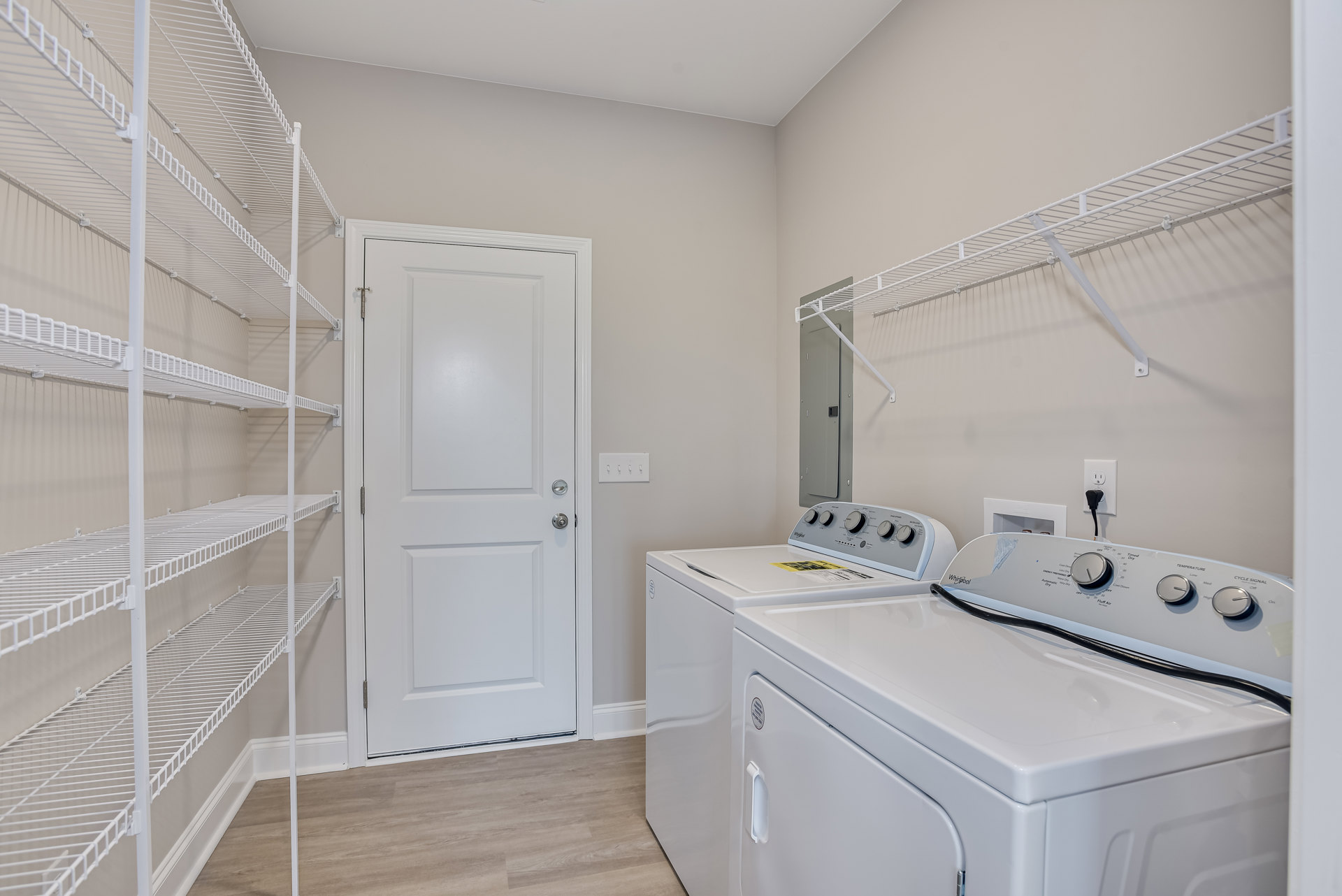 Laundry room with white cabinetry, front-loading washer and dryer, white door with silver hardware, open shelving above appliances, light-colored walls