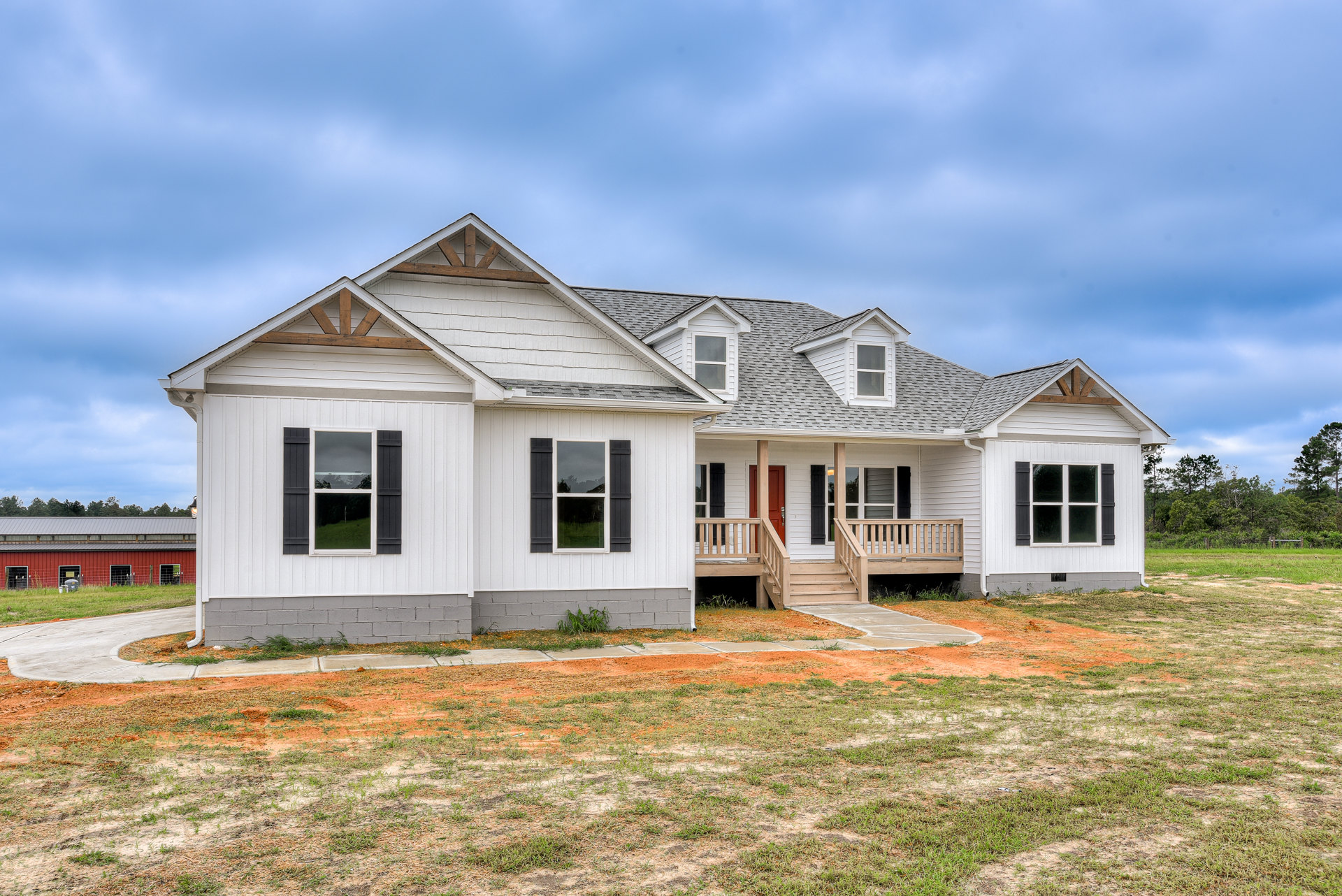 Two-story home with white siding, gray shingle roof, covered front porch, white-framed windows, landscaped yard with green grass, driveway, and blue sky with scattered clouds