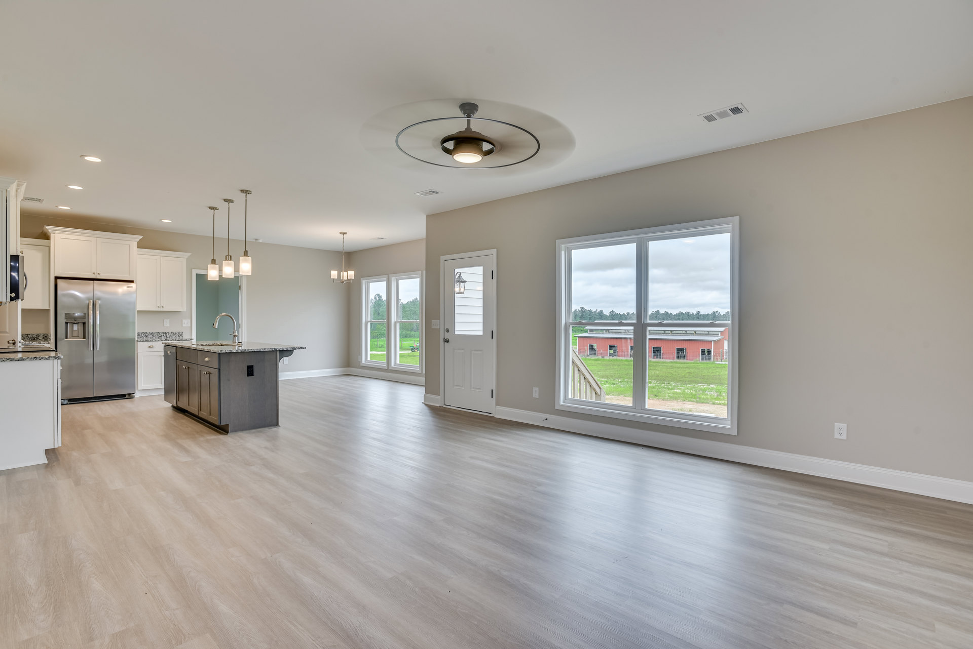 Open-concept kitchen and dining area with laminate flooring, stainless steel refrigerator with water dispenser, white cabinetry, stone countertops, ceiling fan with light, window
