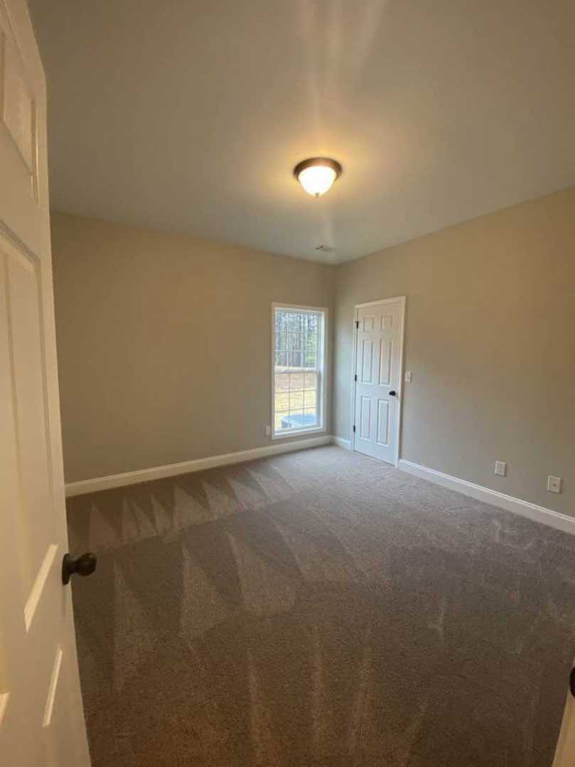 Carpeted room with white paneled door featuring black knobs, window with clear glass pane, white walls with crown molding, and ceiling-mounted light fixture