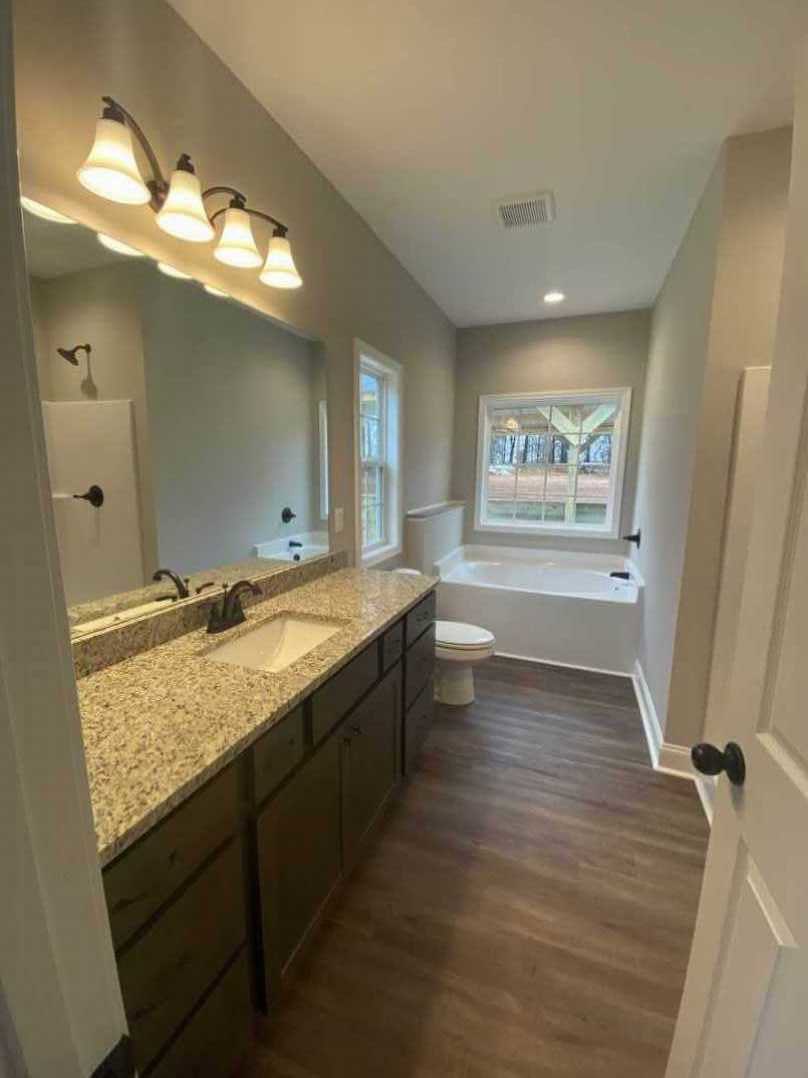 Bathroom featuring marble countertop with white sink and black faucet, freestanding bathtub, white toilet, window with outdoor view, and modern multi-bulb light fixture