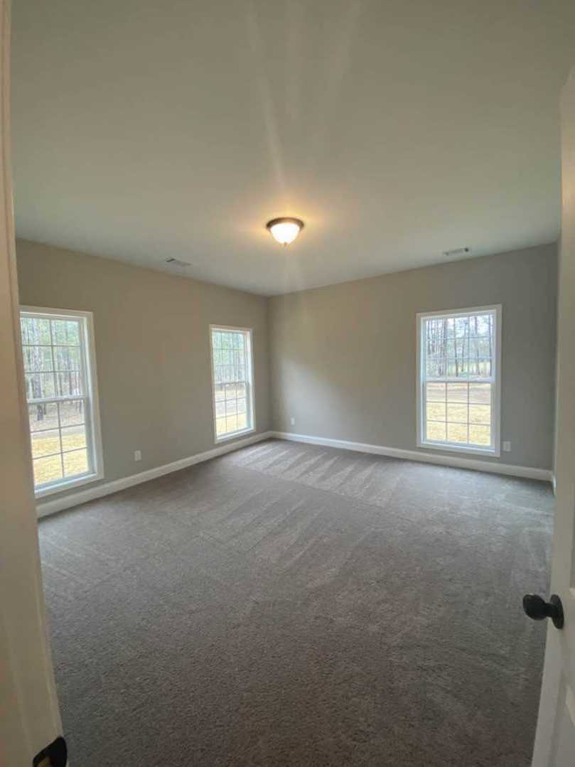 Carpeted room with large windows overlooking trees and a fence, modern ceiling light fixture, white plaster walls