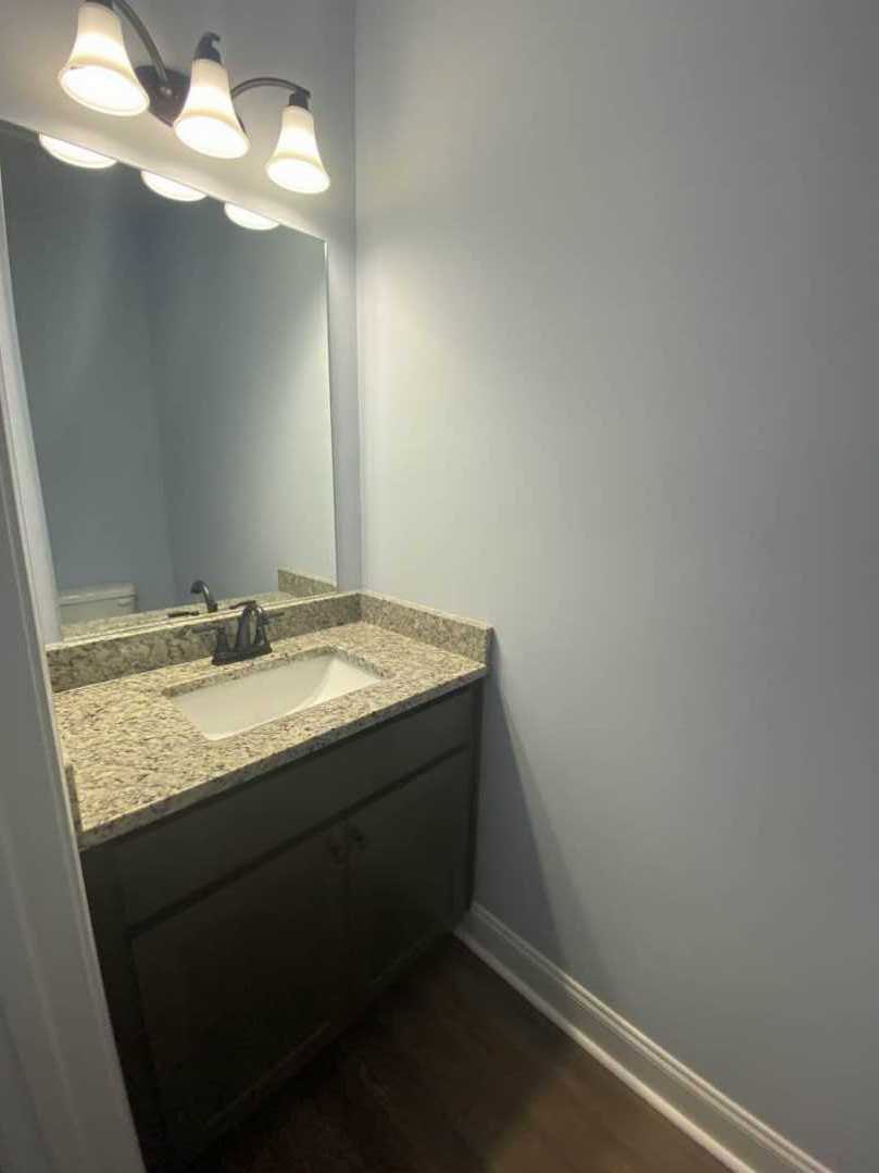 White tile bathroom with rectangular mirror above modern sink and chrome faucet, wall-mounted lighting fixtures, and stone countertop