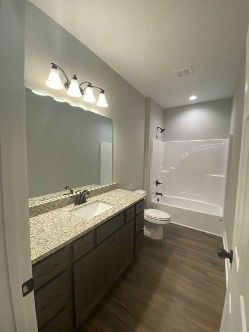Modern bathroom with white porcelain sink, chrome faucet, white toilet, light fixture with multiple bulbs, tiled floor, and neutral wall finishes