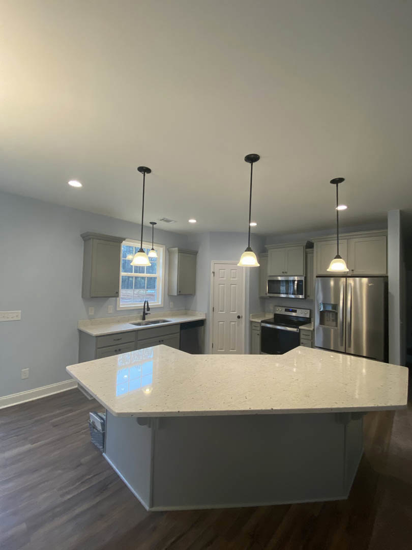 White quartz countertop with undermount sink, stainless steel refrigerator, white cabinetry with black hardware, tile backsplash, and microwave; white door visible in background.