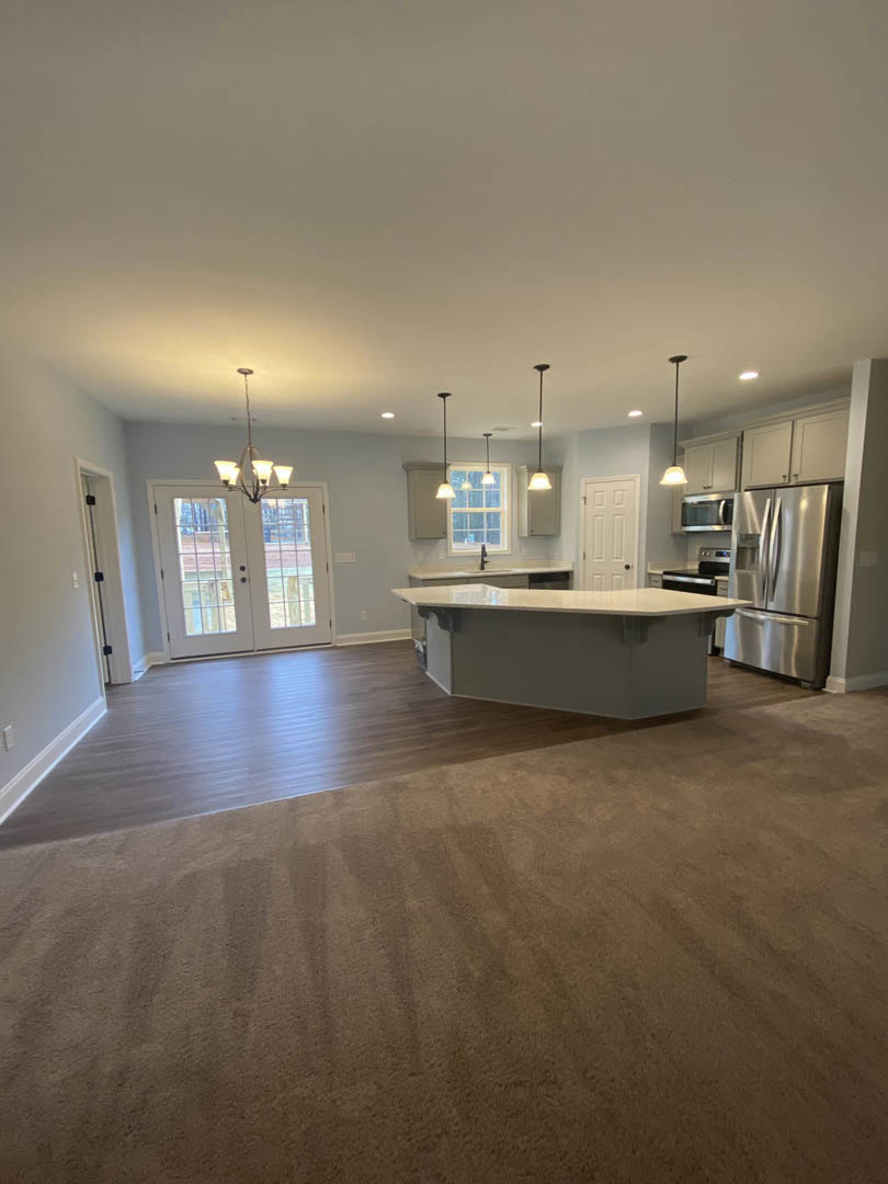 Open-concept kitchen and dining area featuring a large white island with a quartz countertop, stainless steel refrigerator, glass-paneled double doors, white cabinetry, laminate