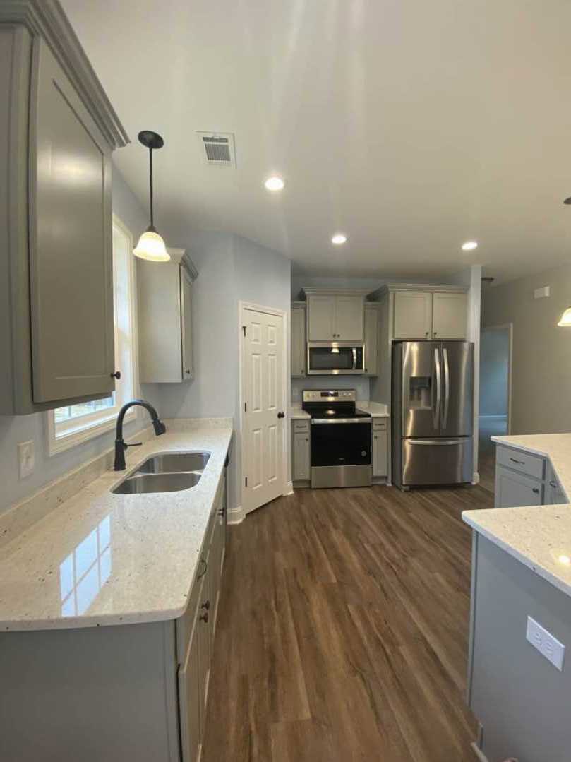 White kitchen with granite countertops, stainless steel stove and refrigerator, wood flooring, white cabinetry with black knobs, and a white door.
