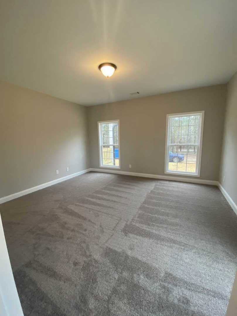 Carpeted room with two white-framed windows, ceiling light fixture, and neutral plaster walls.