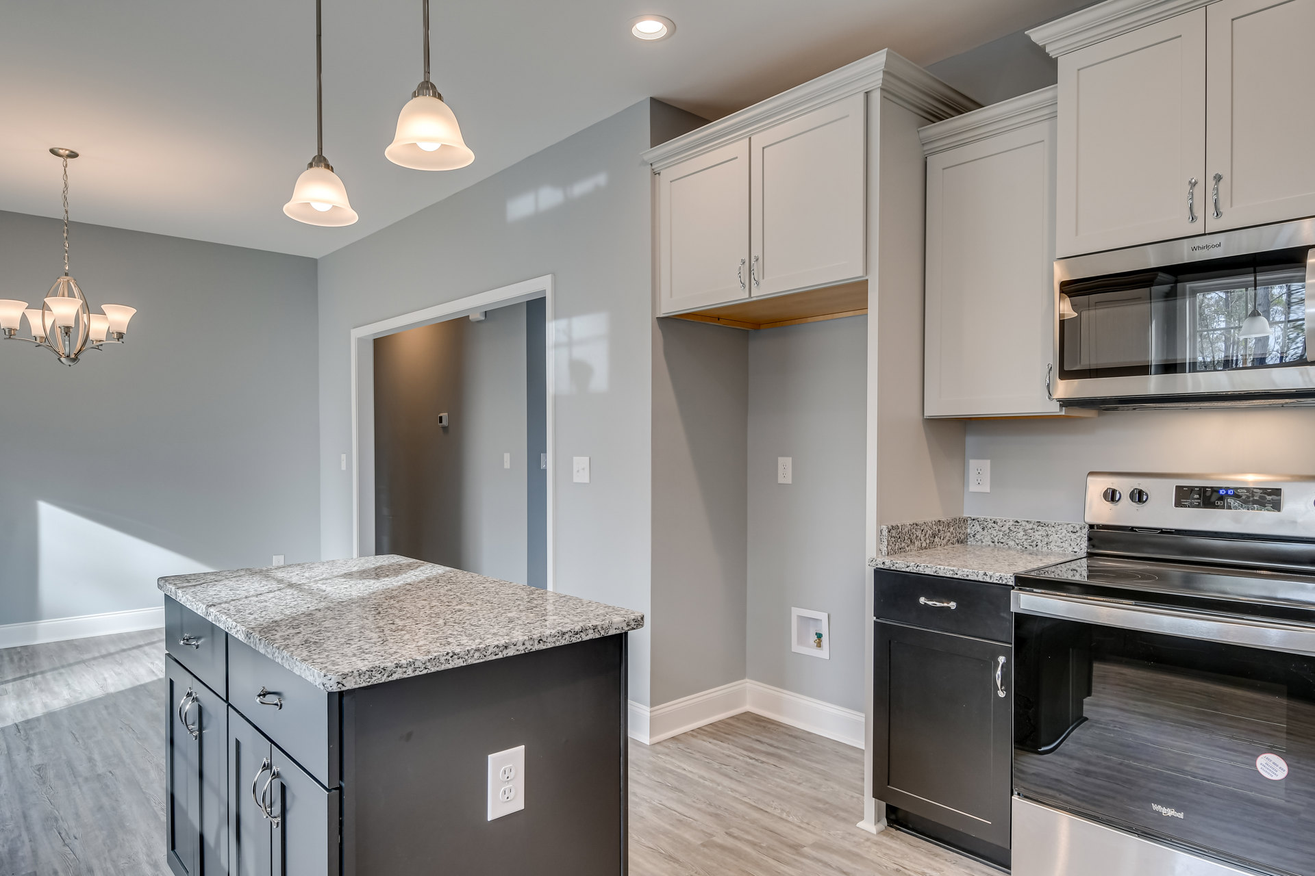 Granite kitchen island with dark wood cabinetry, stainless steel microwave, white electrical outlet, pendant light fixture, and light-colored walls