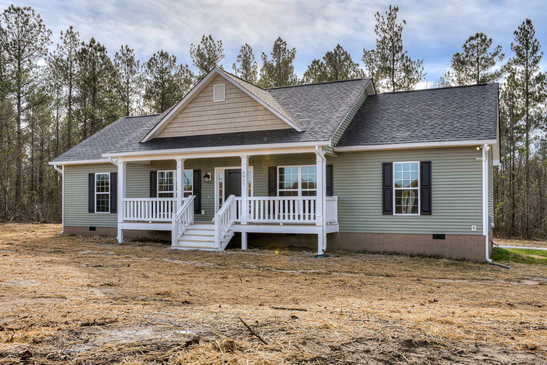 Two-story home with white siding, covered front porch, white railings and stairs, grassy yard, mature trees, and a smaller white house visible in the background