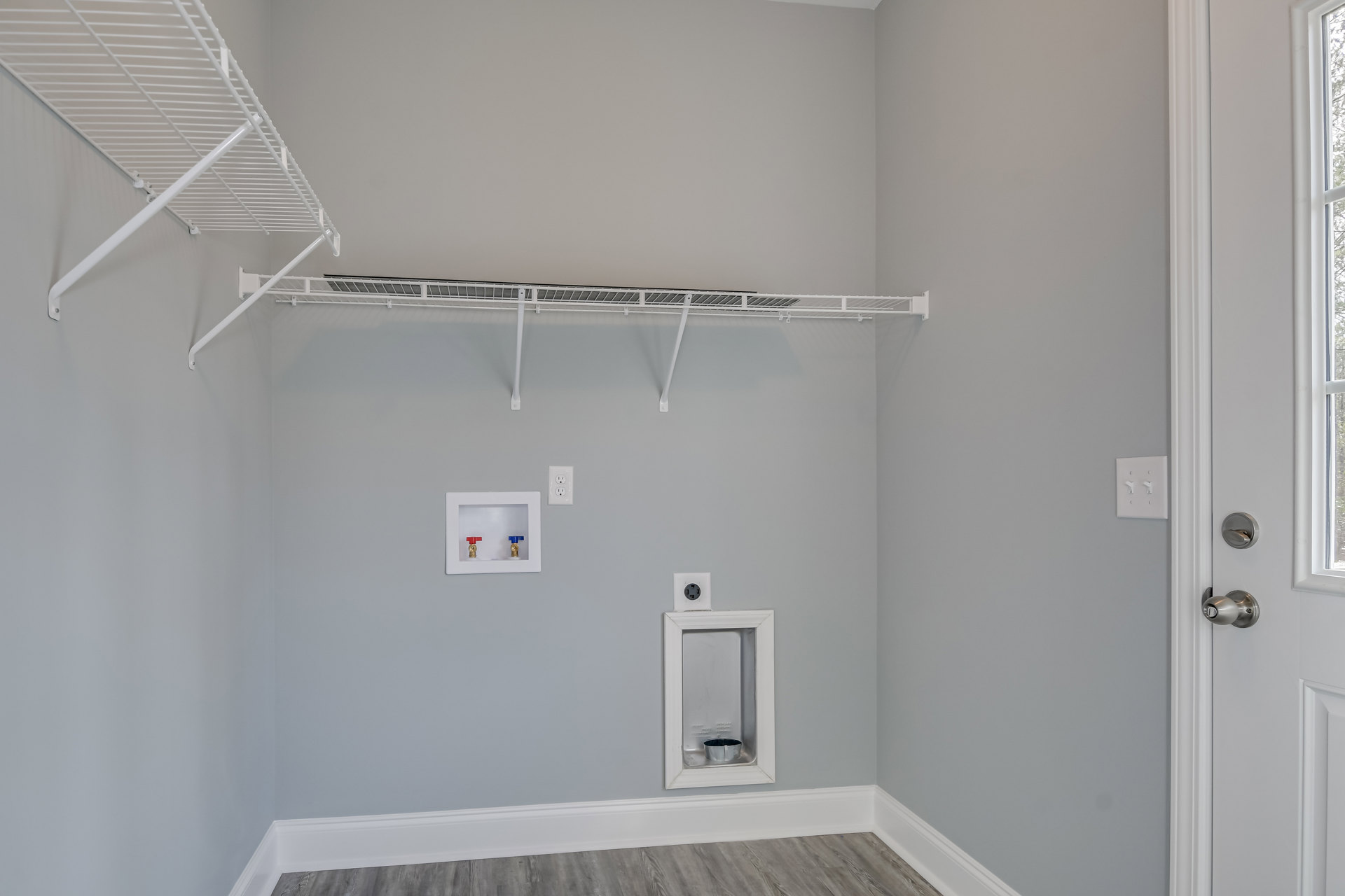 White plaster bathroom with built-in white shelves, wall-mounted light switch, small hole in wall, and white box containing two valves and a measuring cup.