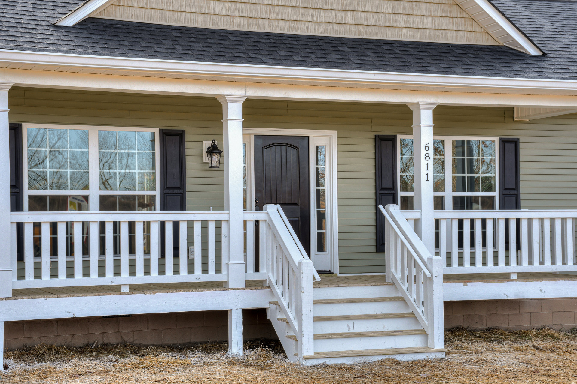 White siding house with covered front porch, black door, white railings, and stairs leading up from landscaped yard.